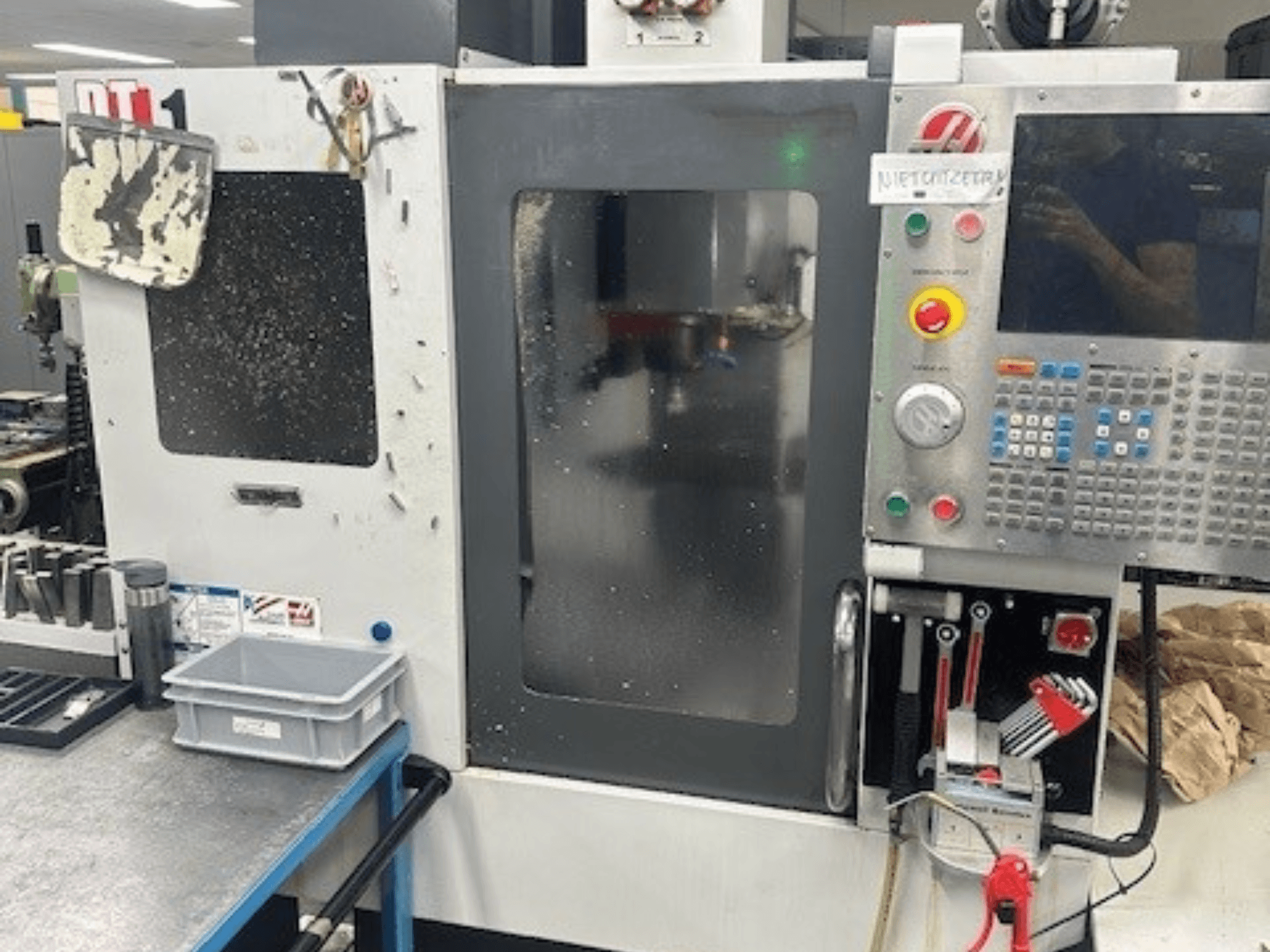 Haas DT-1 Vertikal fleroperationsmaskin, framifrån med kontrollpanel, synlig smuts och verktygsfack på arbetsbänken.