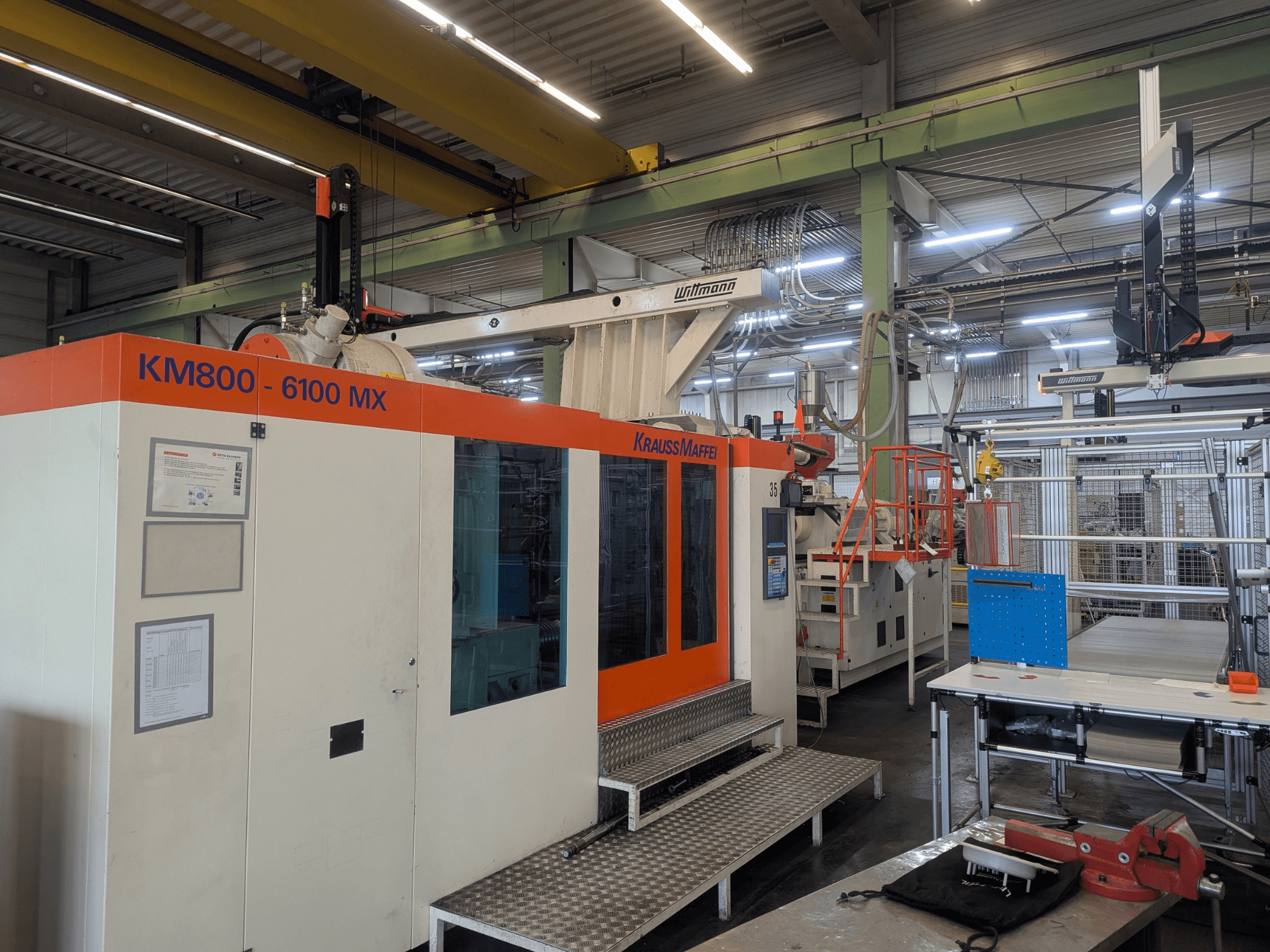 Krauss Maffei KM 800-6100MX hydraulisk formsprutningsmaskin, framifrån, med kontrollpanel och industriell installation.