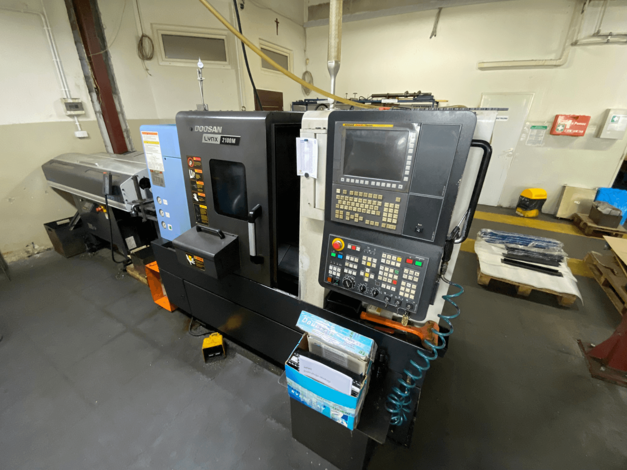 En horisontell svarv av typen DOOSAN LYNX 2100MA sedd från sidan, med kontrollpanel, verktyg och arbetsområde.