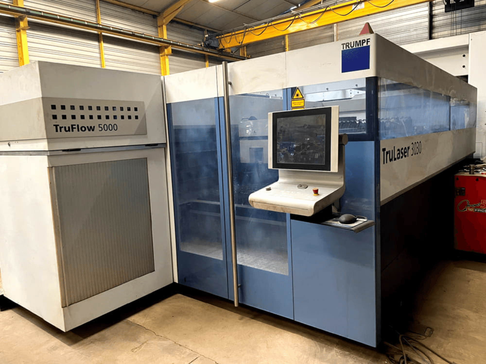 TRUMPF TruLaser 3030 CO₂-laserskärmaskin sett framifrån, med en kontrollpanel och en intilliggande TruFlow 5000-enhet.