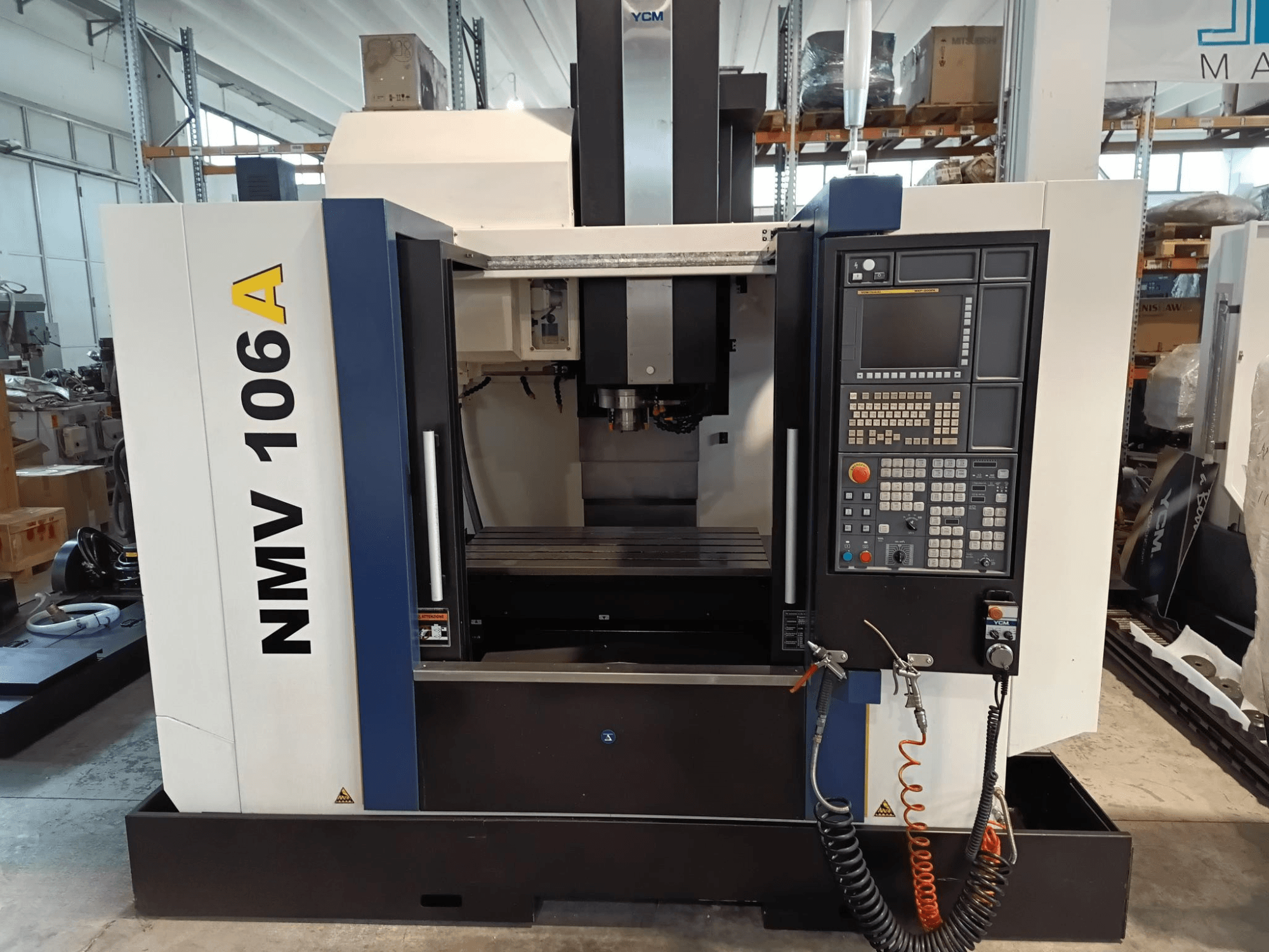 Bearbetningscenter YCM NMV 106A, framifrån, med kontrollpanel med knappar och kylvätskeslangar.