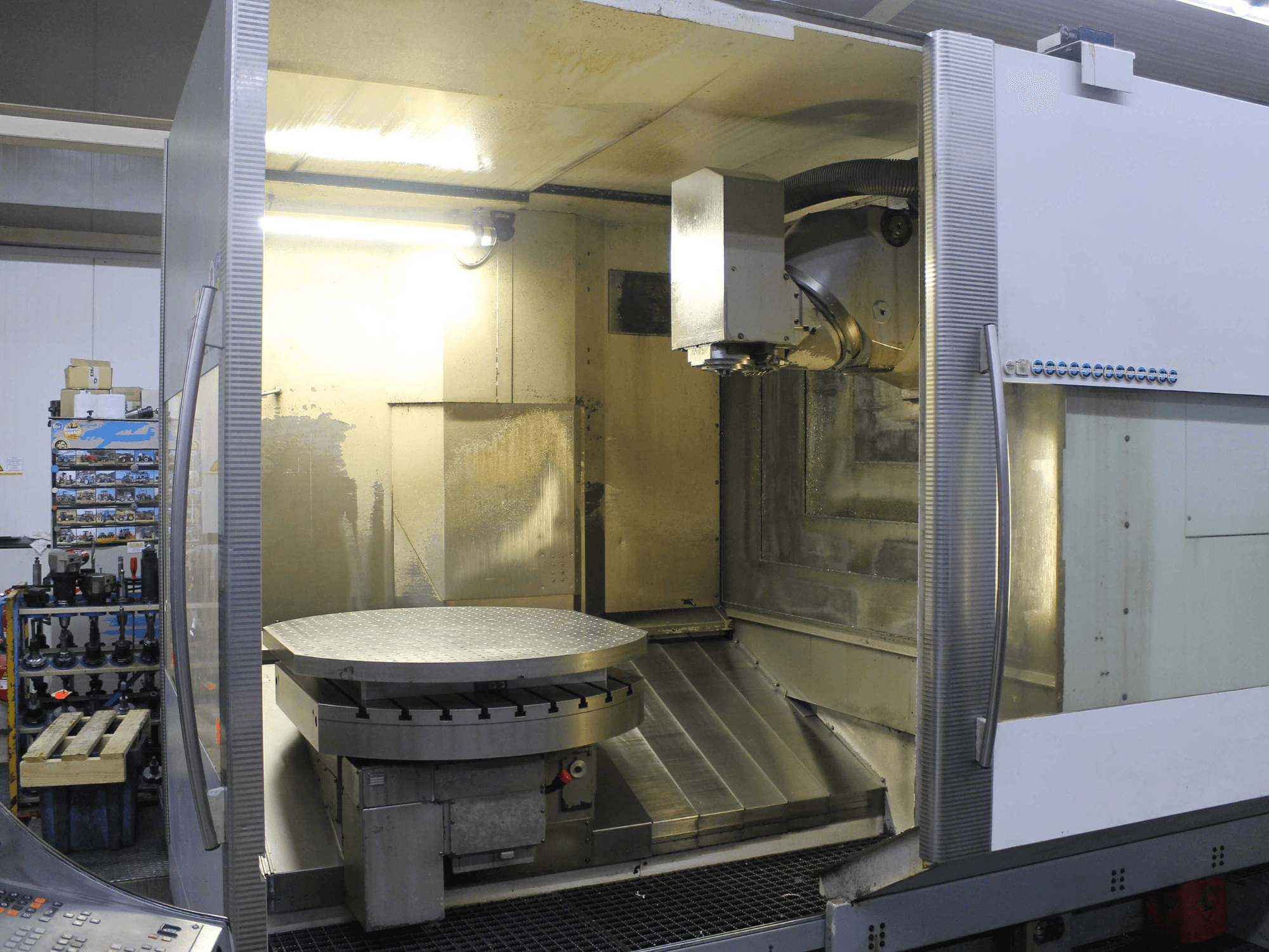 CNC-fräsmaskin med cirkulärt roterande bord och skärhuvud, sedd framifrån, med metalliska ytor och belysning.