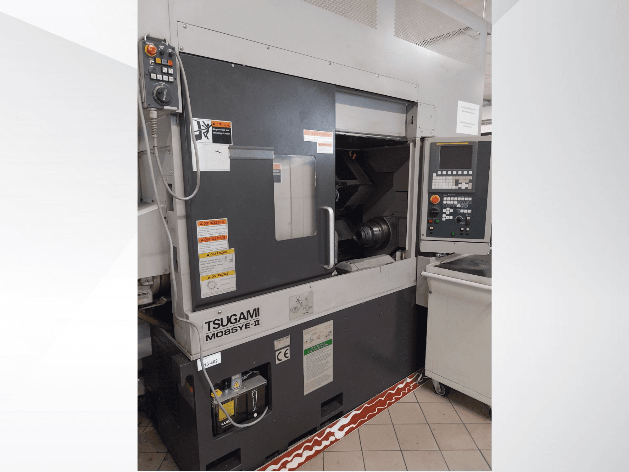Tsugami M08SY-II CNC-svarv, framifrån, med kontrollpanel, spindel och lastutrymme. Med säkerhetsmeddelanden och märkesetikett.