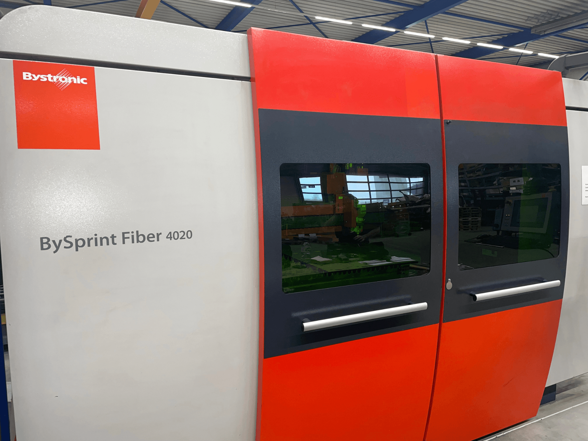 Bystronic BySprint Fiber 4020 framifrån, med en grå och röd paneldesign med stora fönster och kontrollgränssnitt som syns på insidan.