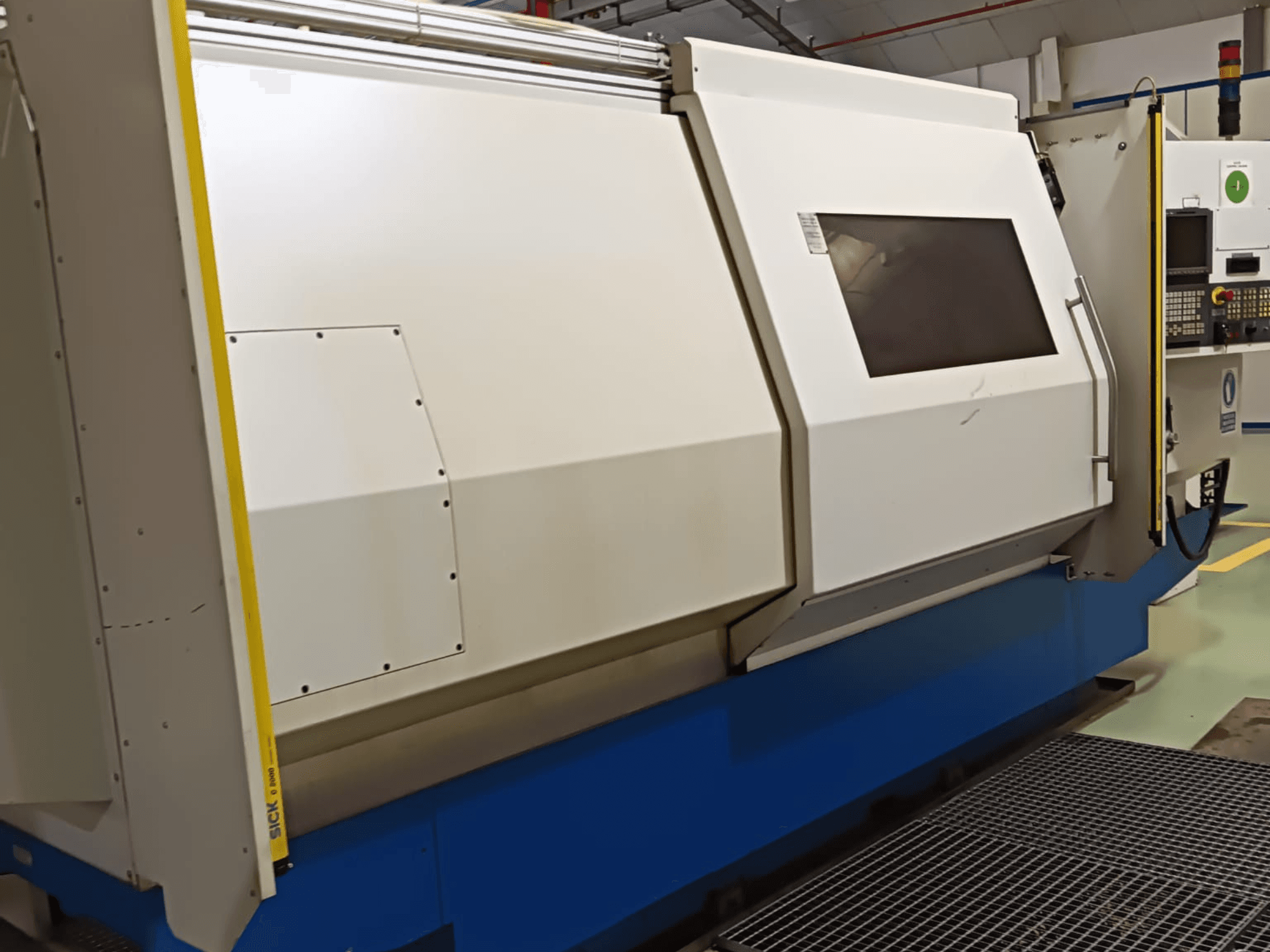 Industriell svarv, vy från sidan, med ett stort vitt och blått hölje, digital kontrollpanel och säkerhetsfunktioner.