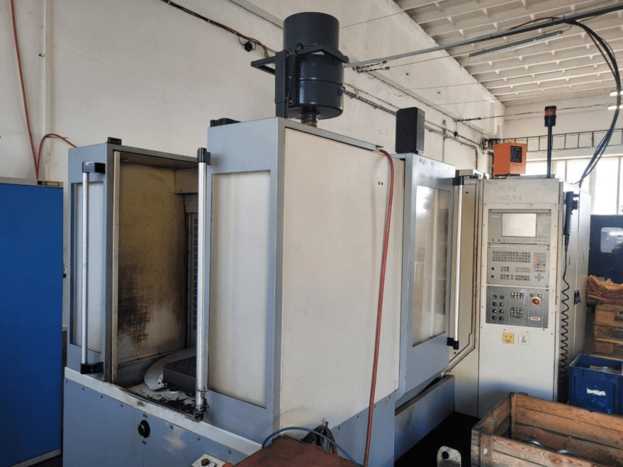 Industriell CNC-fräsmaskin med kontrollpanel, vy från sidan, visar hölje och synlig smuts på ytor.
