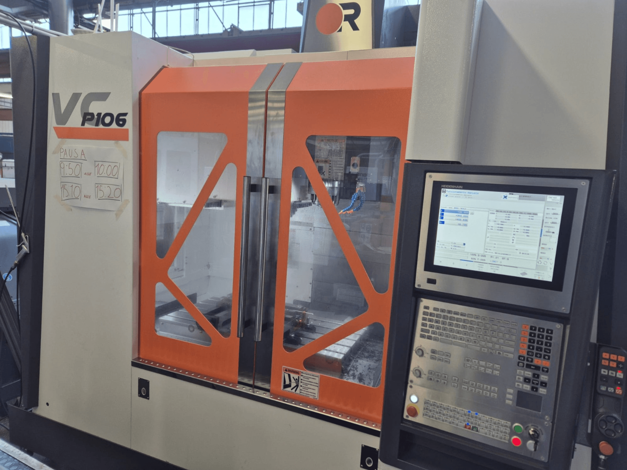 Alt text: Orange och grå VF P106 CNC-maskin, framifrån, visar en kontrollpanel och schemalagda drifttider på papper.