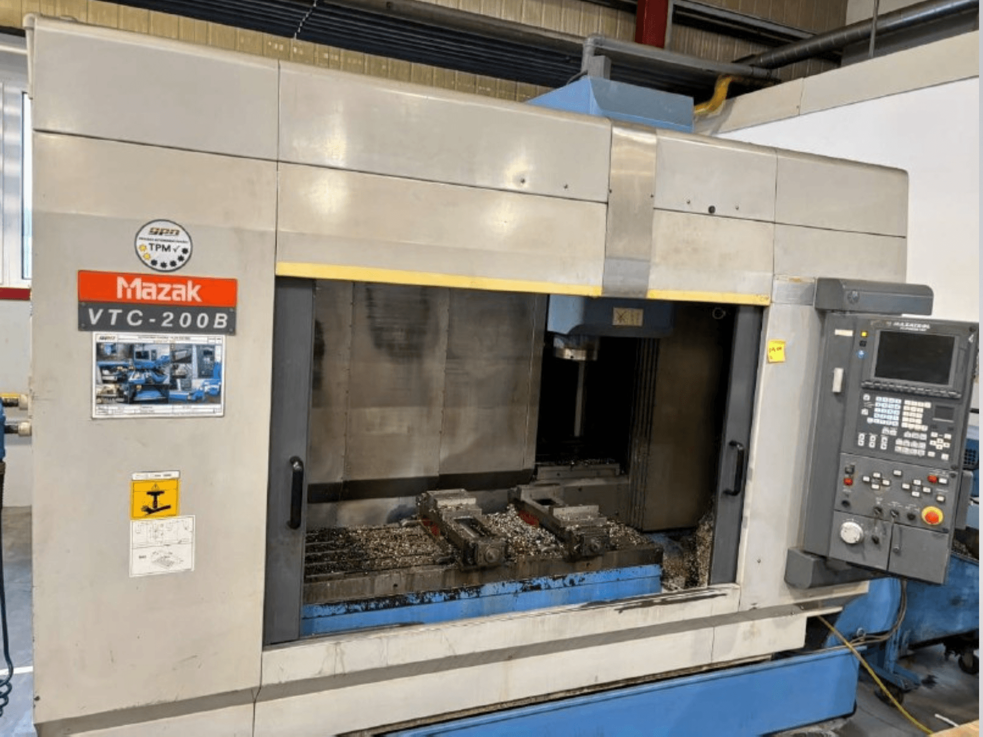 Mazak VTC-200B vertikal bearbetningscenter, sidovy med synlig kontrollpanel och metallspån i arbetsområdet.