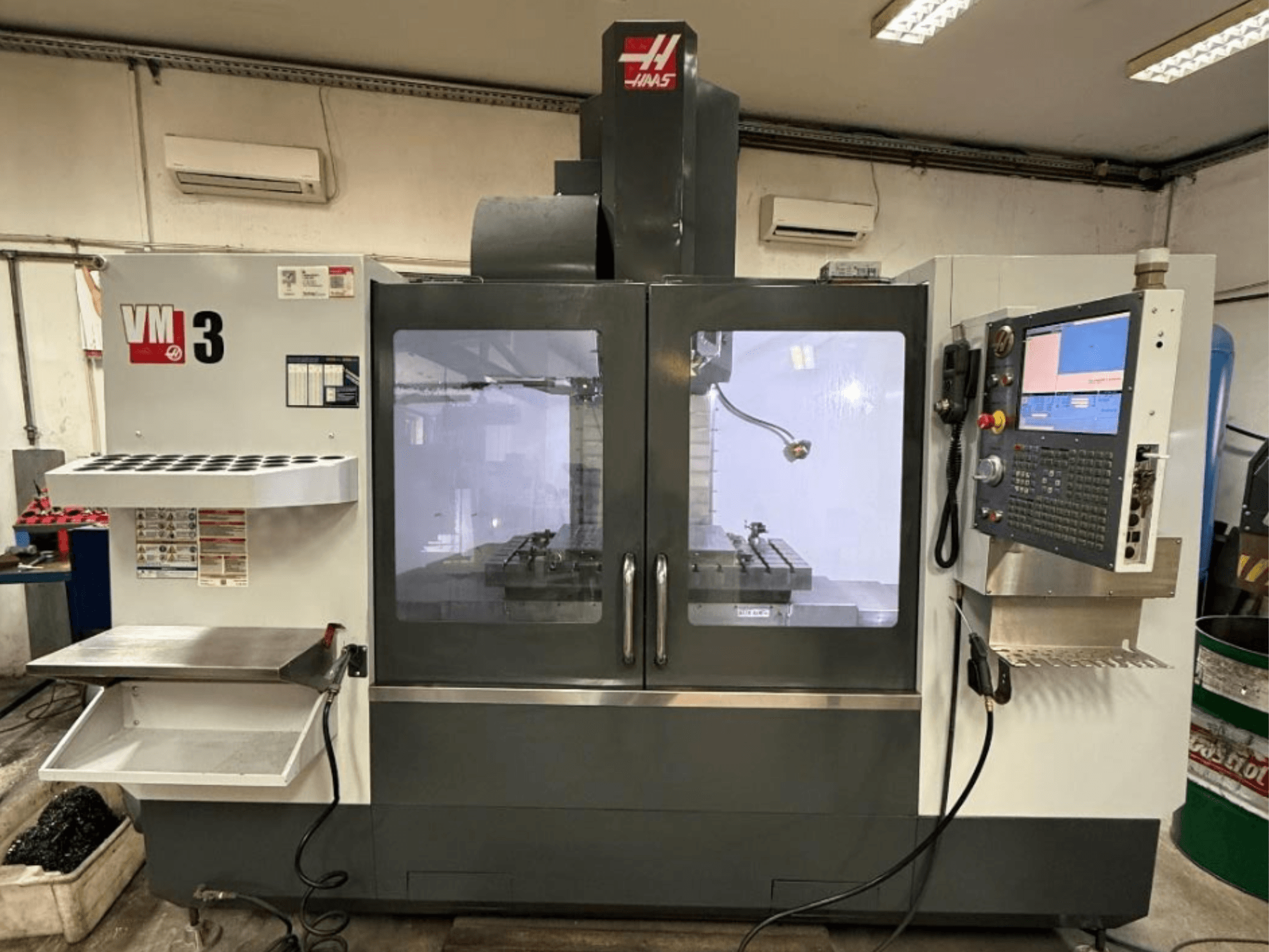 Haas VM-3 vertikalt bearbetningscenter sett framifrån, med en stor kontrollpanel och ett synligt arbetsområde med verktyg.