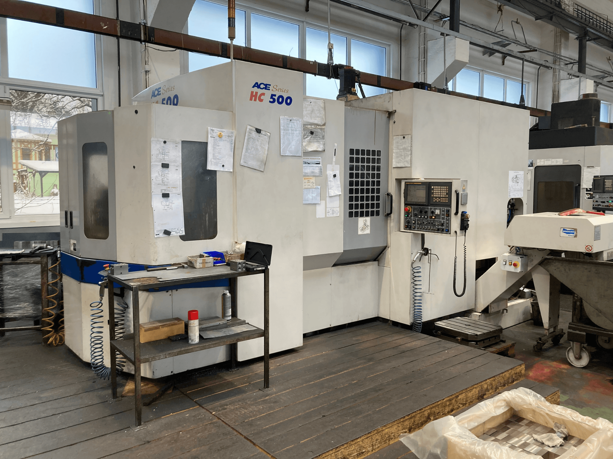 DOOSAN ACE HC-500 horisontellt bearbetningscenter, framifrån; har kontrollpanel, förvaring av flera verktyg och industriell miljö.