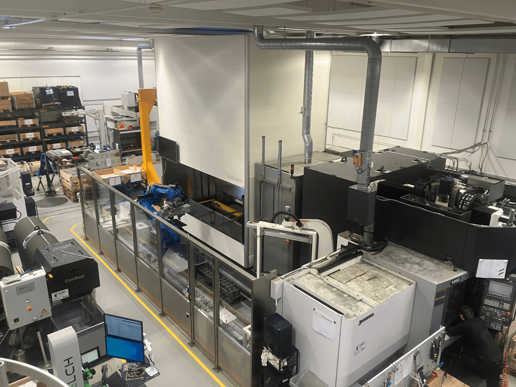 SSI SCHAFER Logimat automationssystem i ett lager, vy framifrån; med robotarm, lagerhyllor och maskiner.