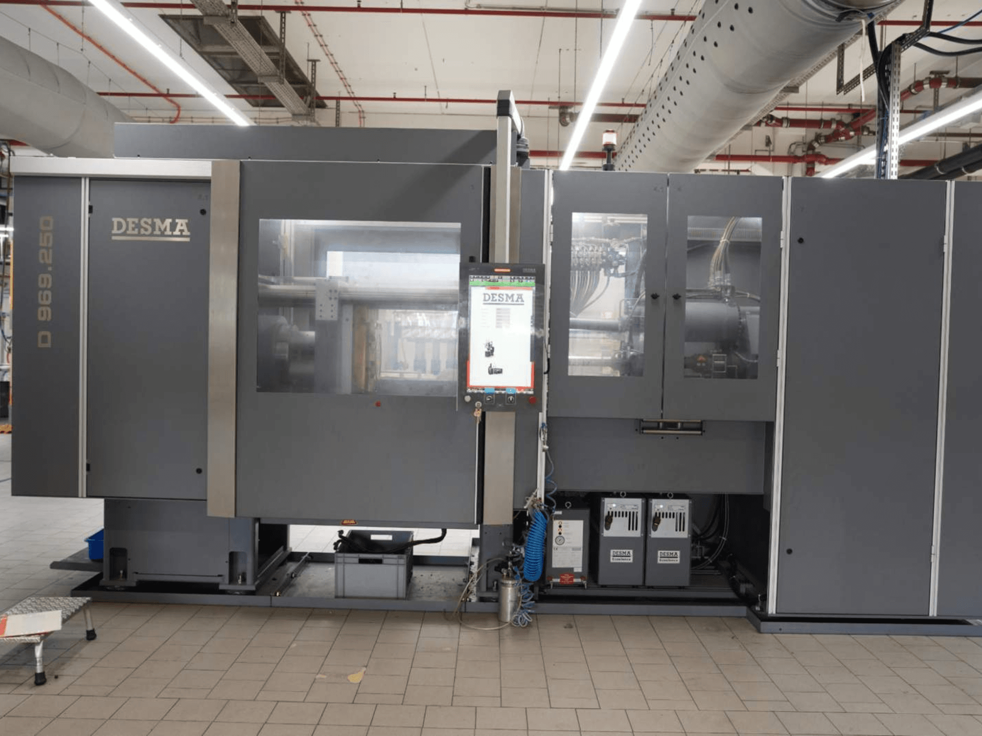 Vertikal formsprutningsmaskin Kloeckner Desma D 969.250 Z (S3) i fabriksmiljö, framifrån med kontrollpanelen.