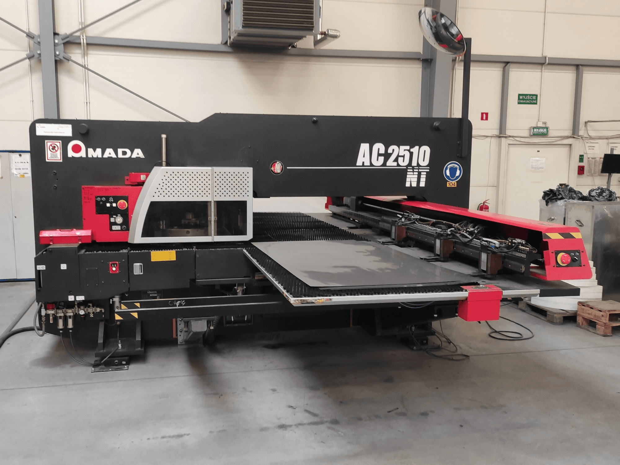 Amada AC2510 NT CNC-stansmaskin, framifrån, med kontrollpanel och lastningsområde för plåt.