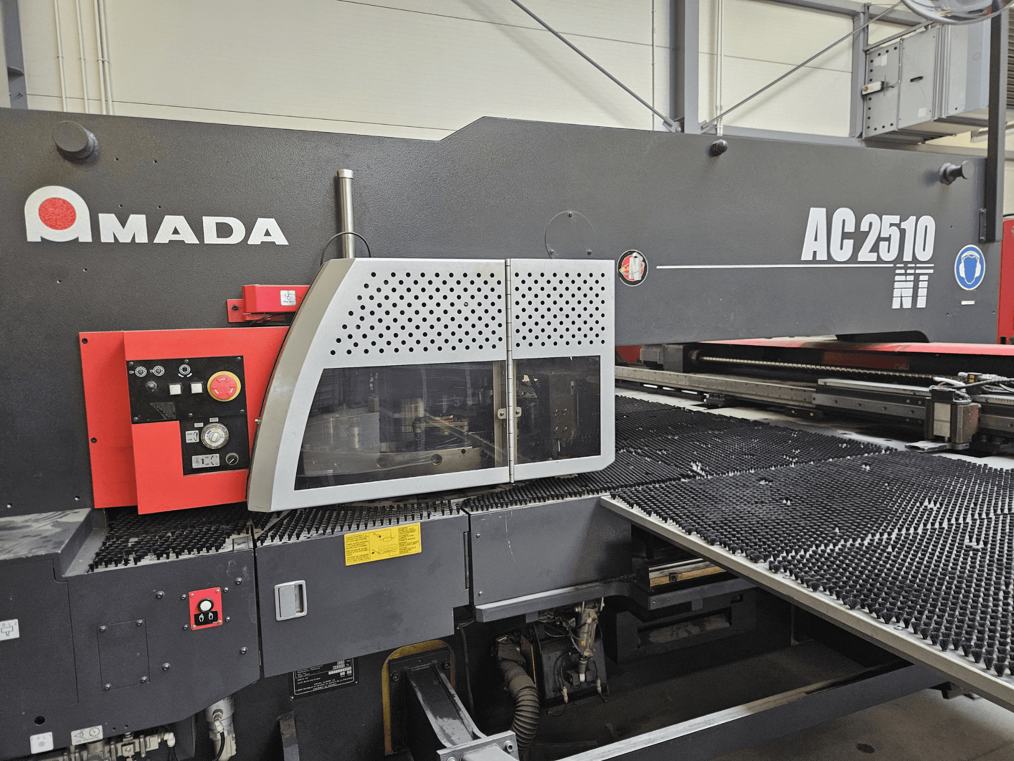 Amada AC2510 NT laserskärmaskin, framifrån, med kontrollpanel med vred, knappar och ett säkerhetsskydd.