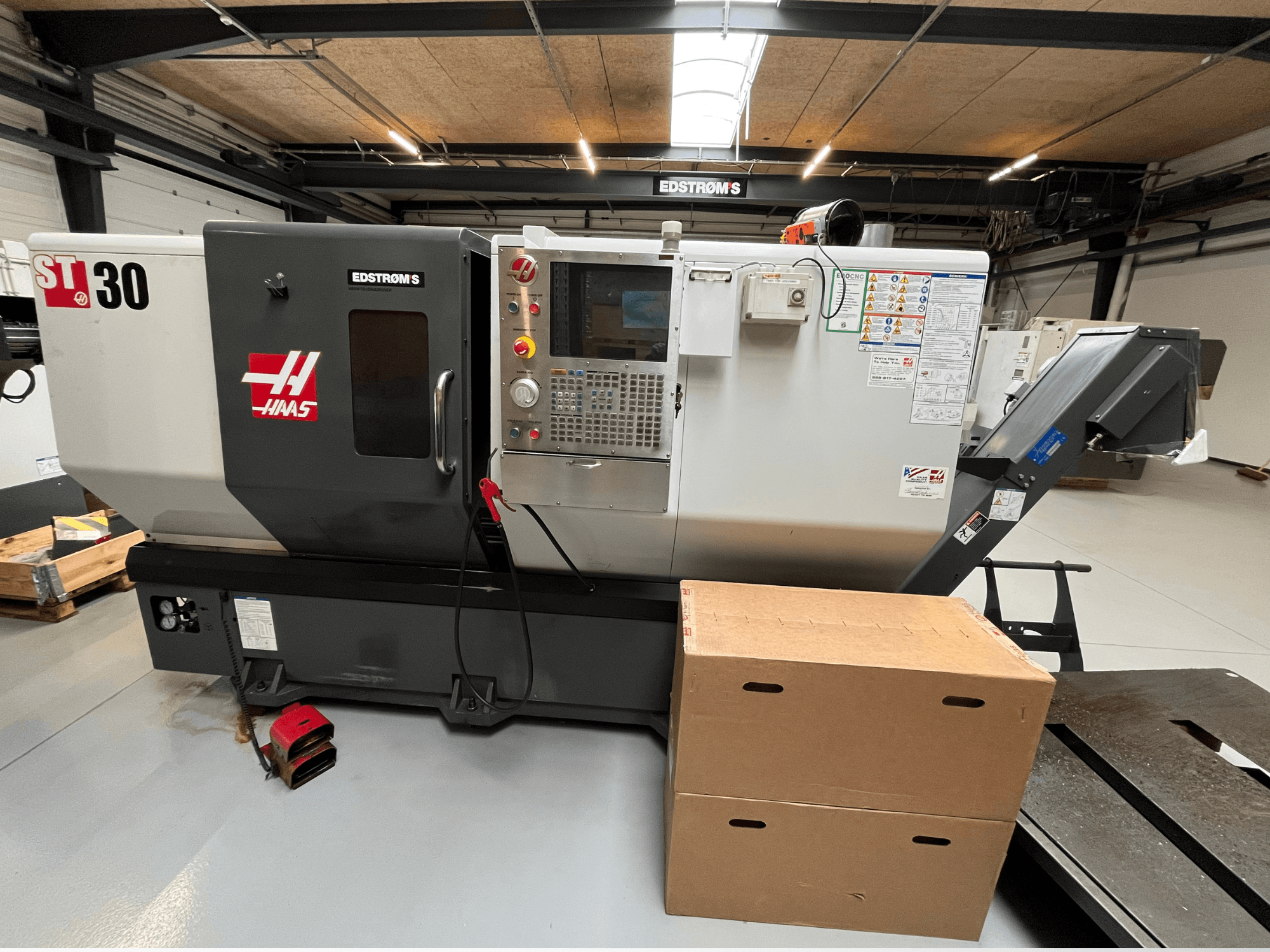 Haas ST-30 CNC-svarv sedd från sidan, med en kontrollpanel, modellmärke och två kartonger i närheten.