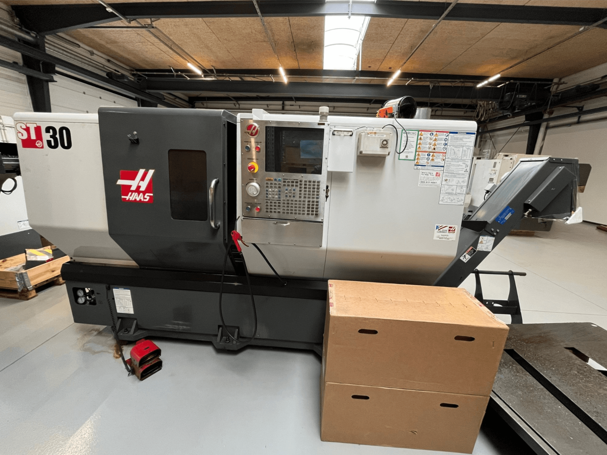 Haas ST-30 CNC-svarv, framifrån, med kontrollpanel med knappar, nödstopp och två staplade kartonger.