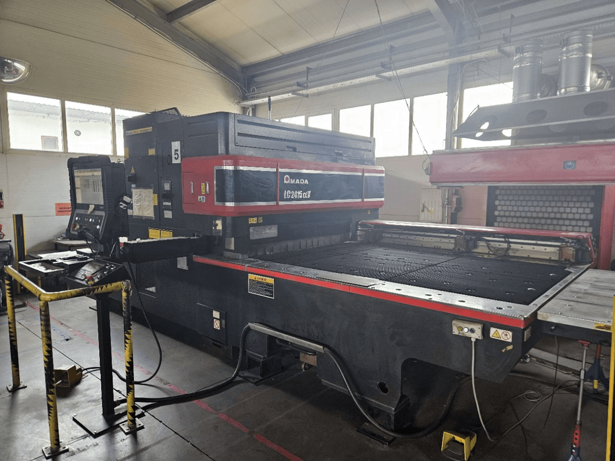 AMADA LC2415 Alpha 5 CO₂-laserskärmaskin, framifrån sett med kontrollpanel och skärbord med säkerhetsbarriärer.