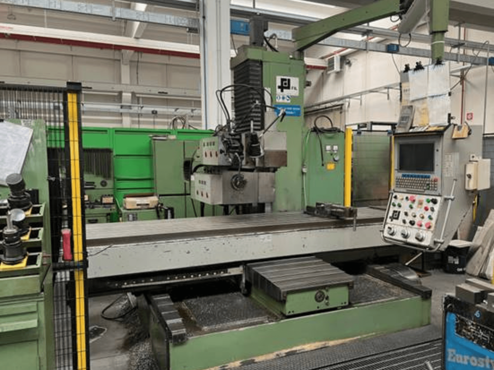 Industriell fräsmaskin från JFL, framifrån med kontrollpanel, stort plant bord och metallspån på golvet.