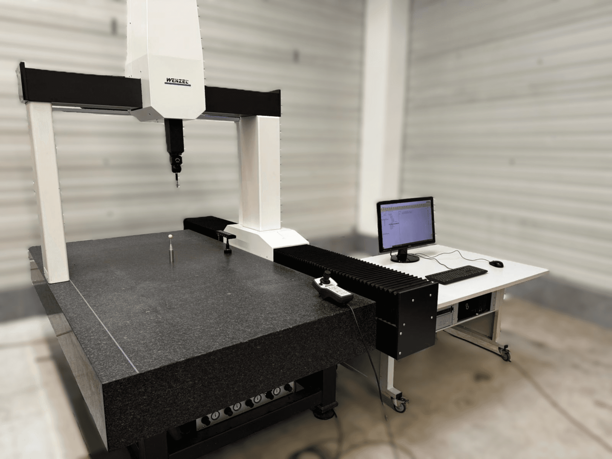 Wenzel XO 87 CMM framifrån, med en mätprob och ett granitbord med en datoruppställning bredvid.