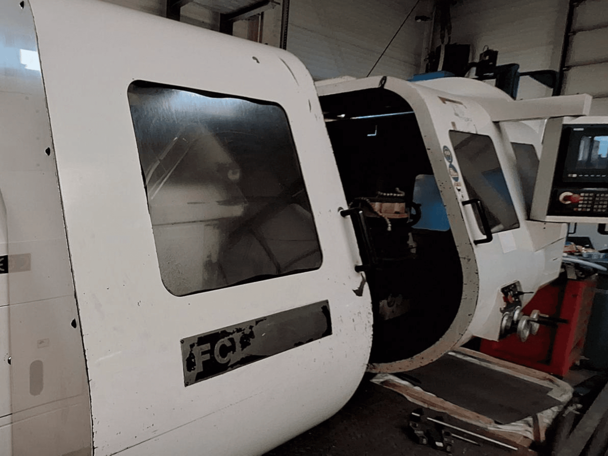 Vit CNC-maskin med synlig kontrollpanel och öppen dörr som visar inre komponenter; vy framifrån. Varumärke: FCT.