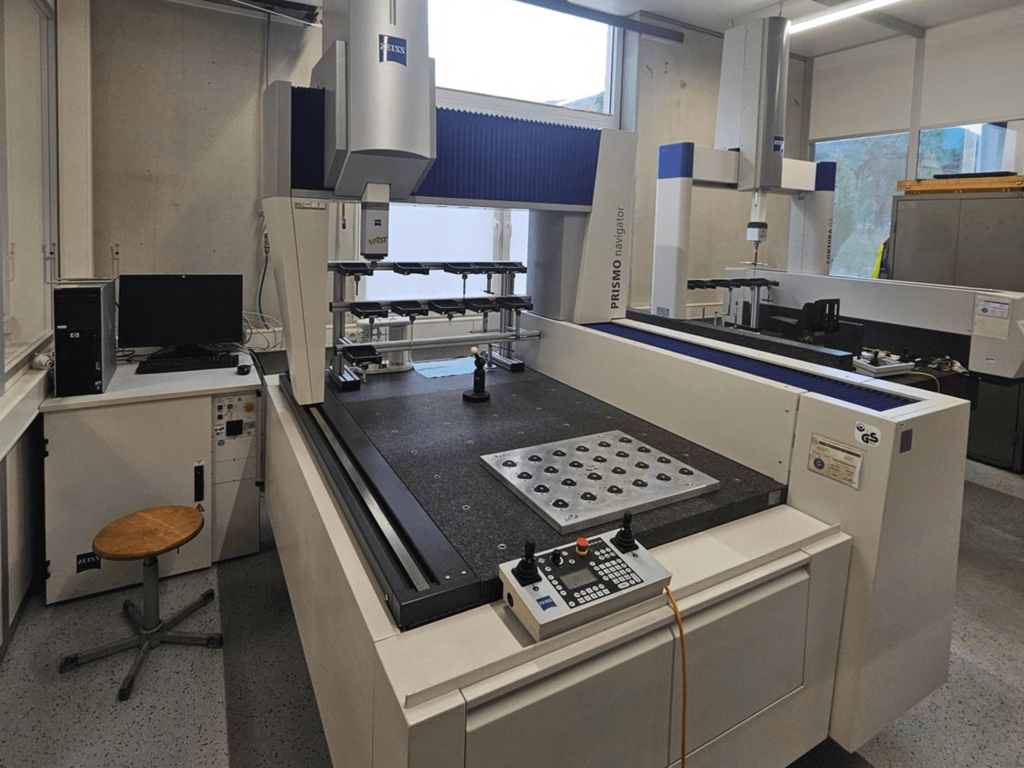 ZEISS Prismo Navigator 7 CMM i ett laboratorium, framifrån sett med kontrollpanel, arbetsbord och bildskärm.