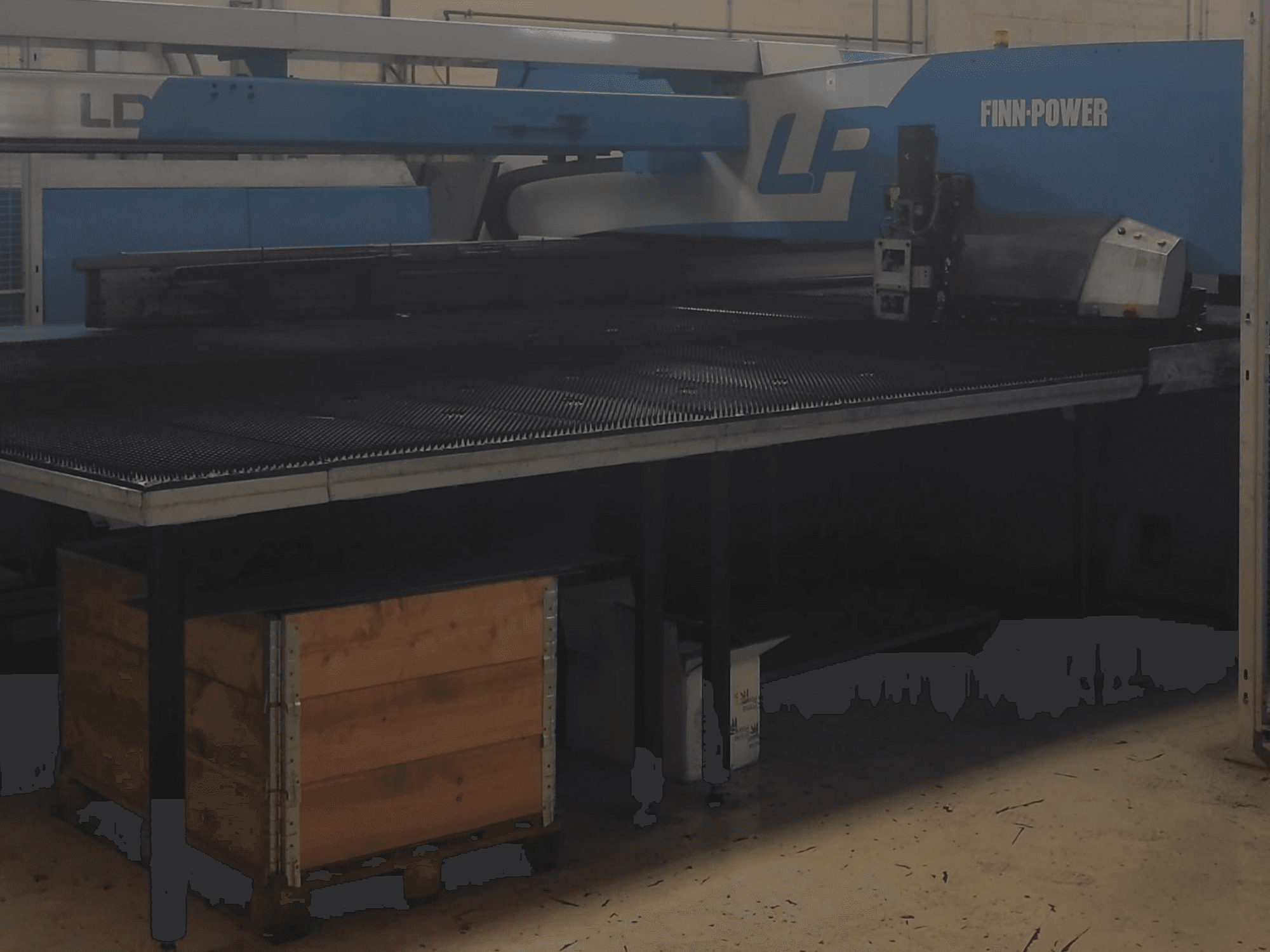 Finn-Power LP-skärmaskin i en fabrik, framifrån med ett bord i strukturerad metall och en trälåda under.