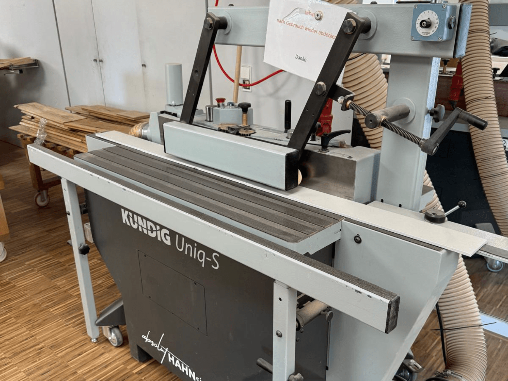 Kundig UNIQ-S bandslip i en verkstad, sidovy som visar slipbandet och de justerbara stödarmarna.