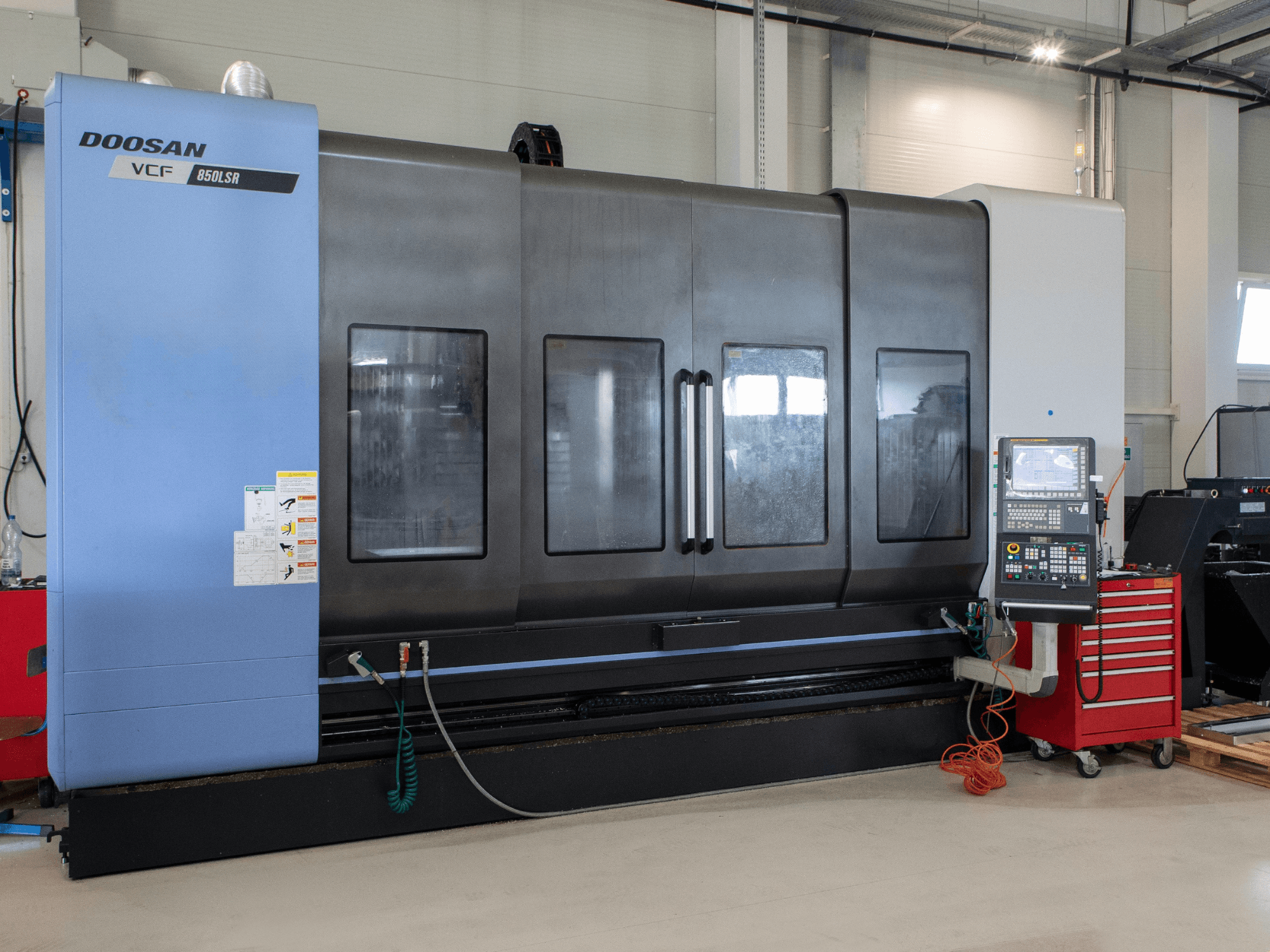 DOOSAN VCF850 fräs- och svarvcenter, framifrån; utrustad med stora dubbla fönster, kontrollpanel och verktygsförvaring. Perfekt för bearbetning.