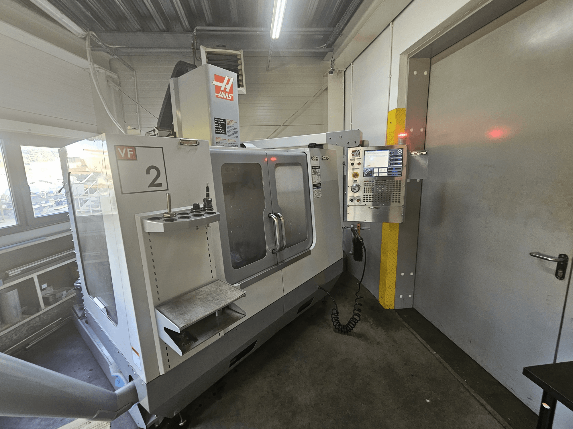Haas VF-2 CNC-fräsmaskin, framifrån, med kontrollpanel, verktygshållare och ett tydligt fönster mot arbetsytan.