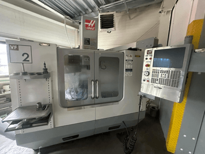 Haas VF-2 CNC-maskin, framifrån, med reglage, verktygshållare och genomskinliga dörrar med synliga verktyg inuti skåpet.