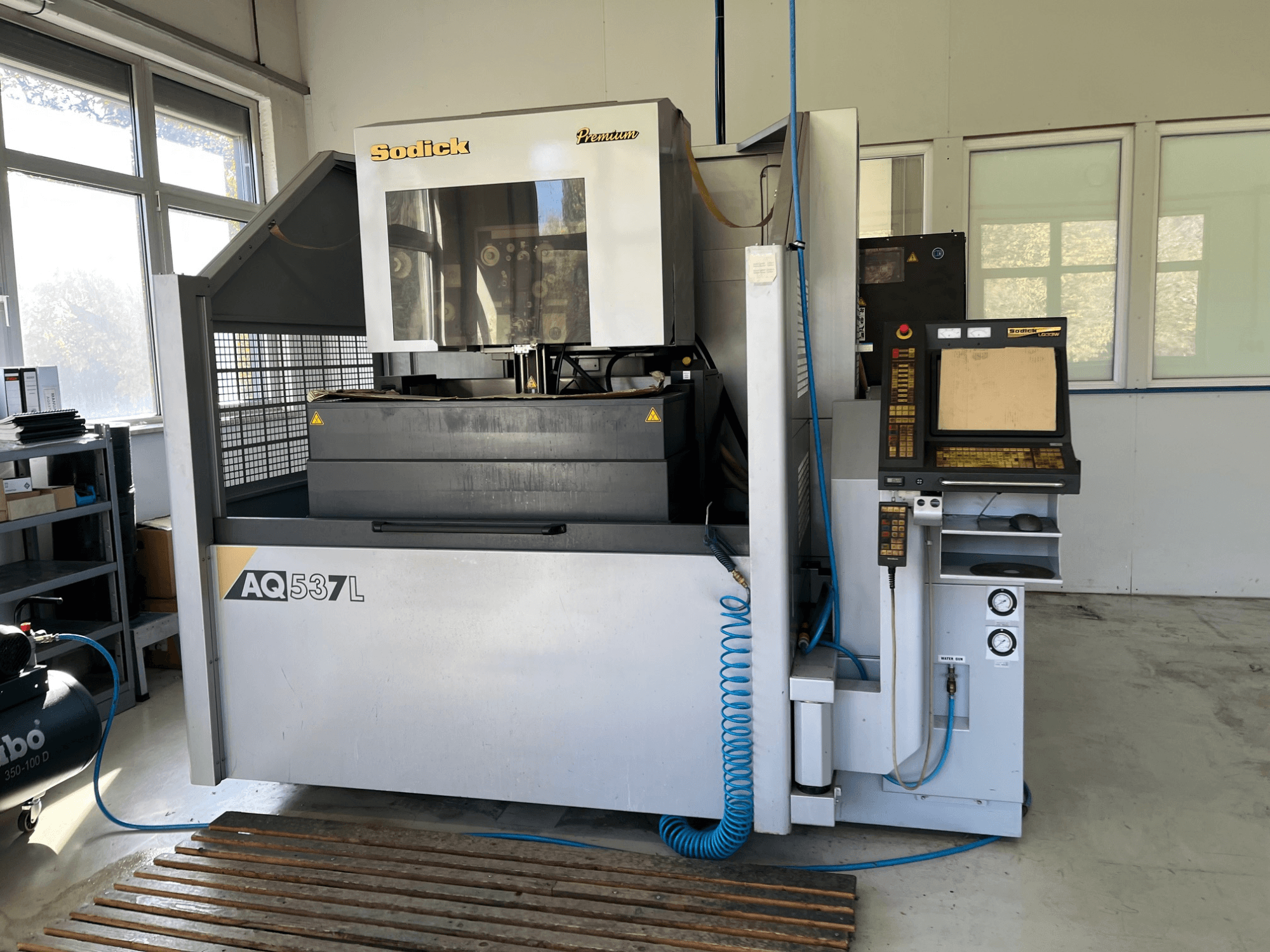 Sodick AQ537L elektrisk gnistbearbetningsmaskin (EDM) framifrån, med kontrollpanel, vattenkylningsledningar och arbetsyta.