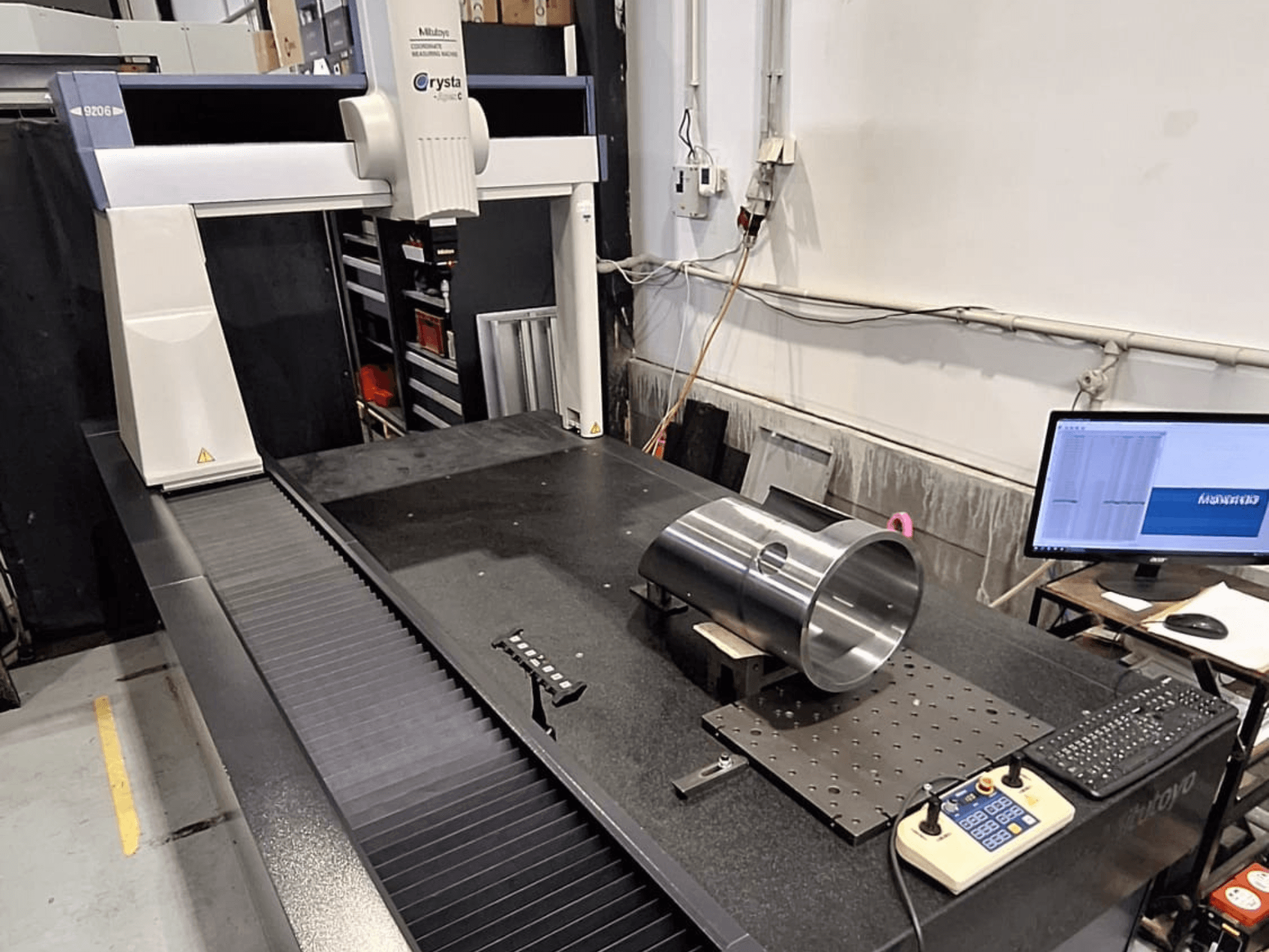 Mitutoyo Crysta-Apex C9206 CMM framifrån, mäter en cylindrisk metalldel på en svart granitplatta.