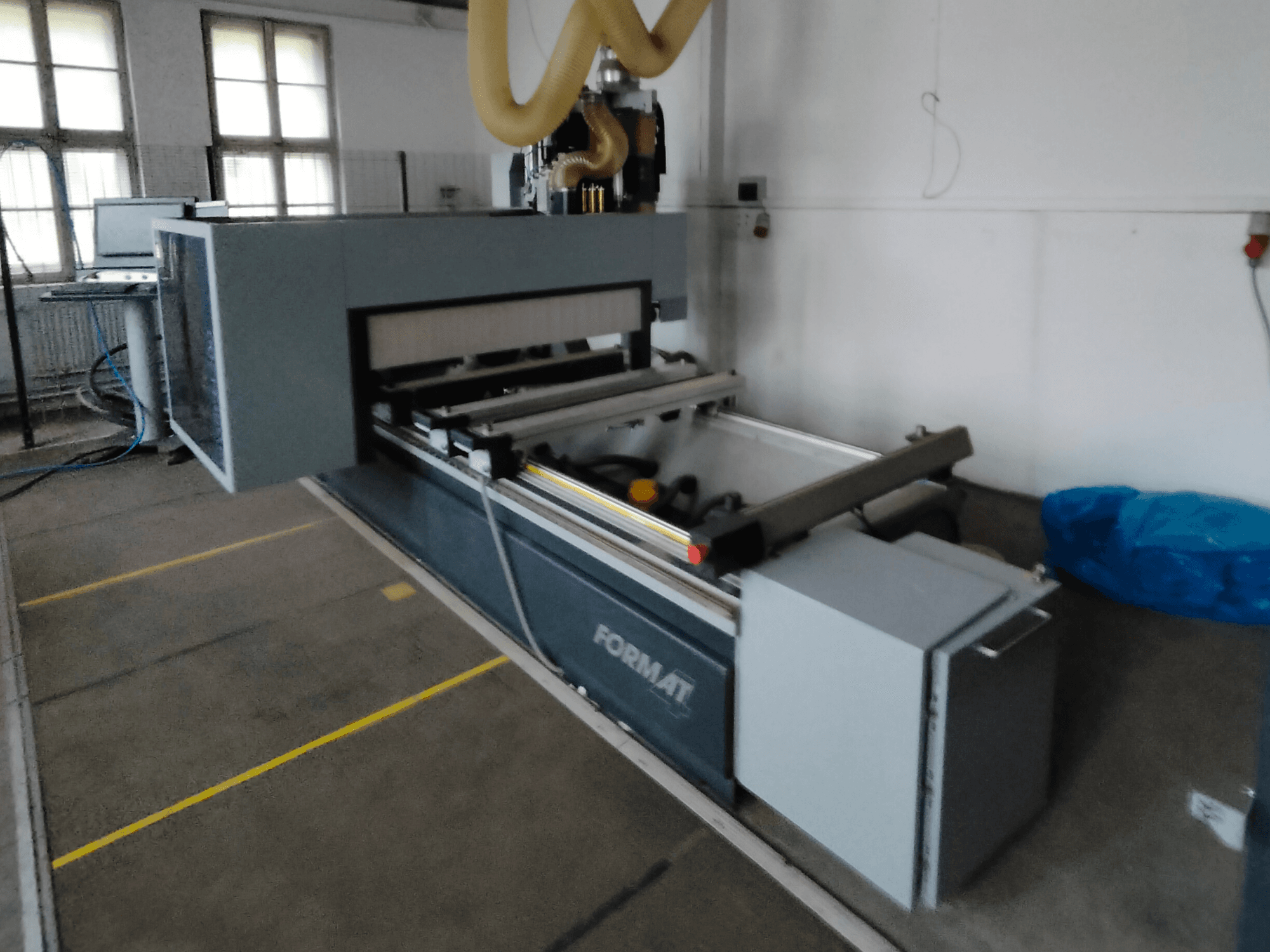 Frontvy av en Format CNC-maskin med grå stomme, styrskenor och synlig manöverpanel.