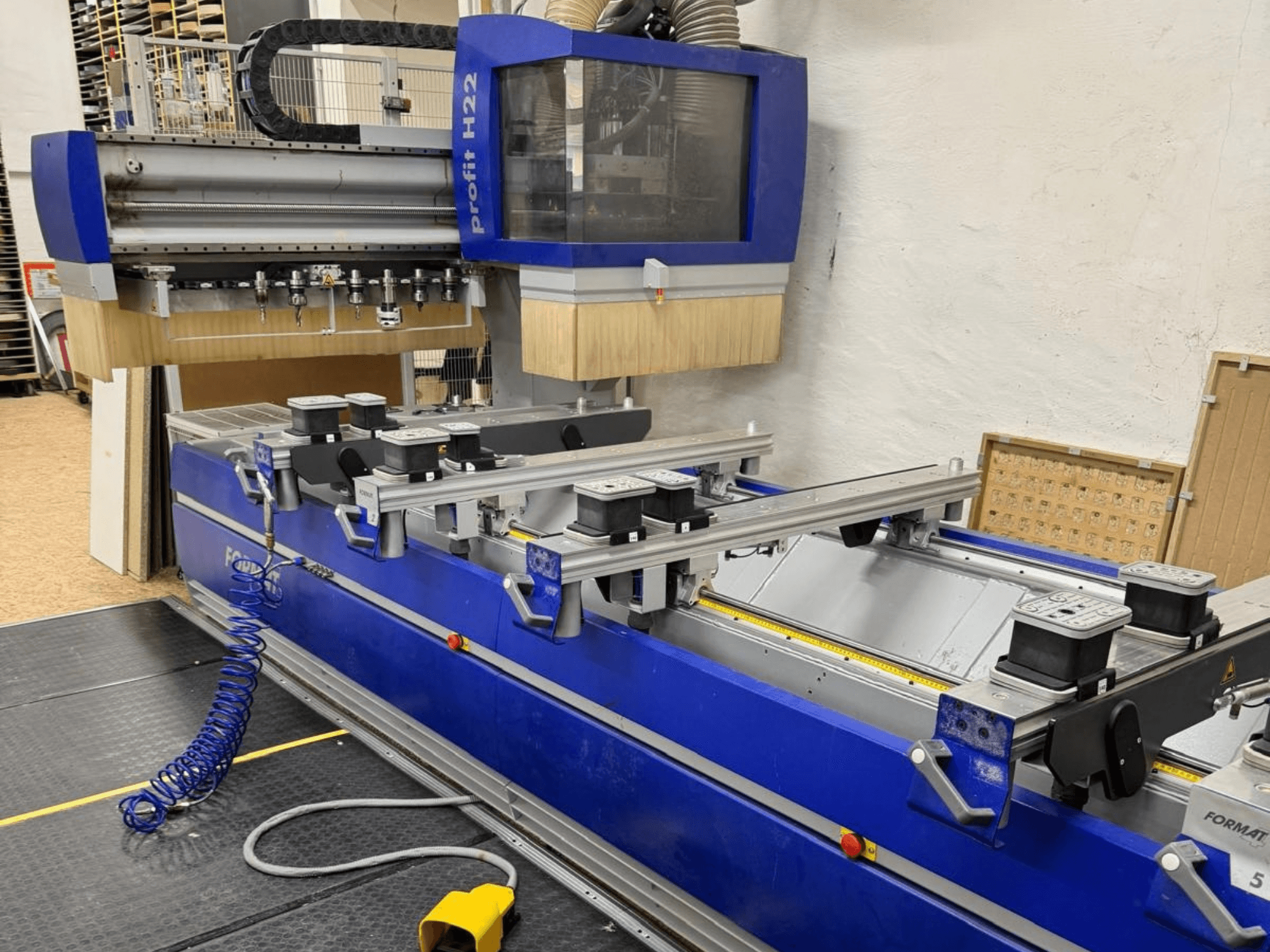 FORMAT4 PROFIT H22 CNC-bearbetningscenter för trä, framifrån, med bearbetningsverktyg och spännklämmor synliga på den blå karossen.