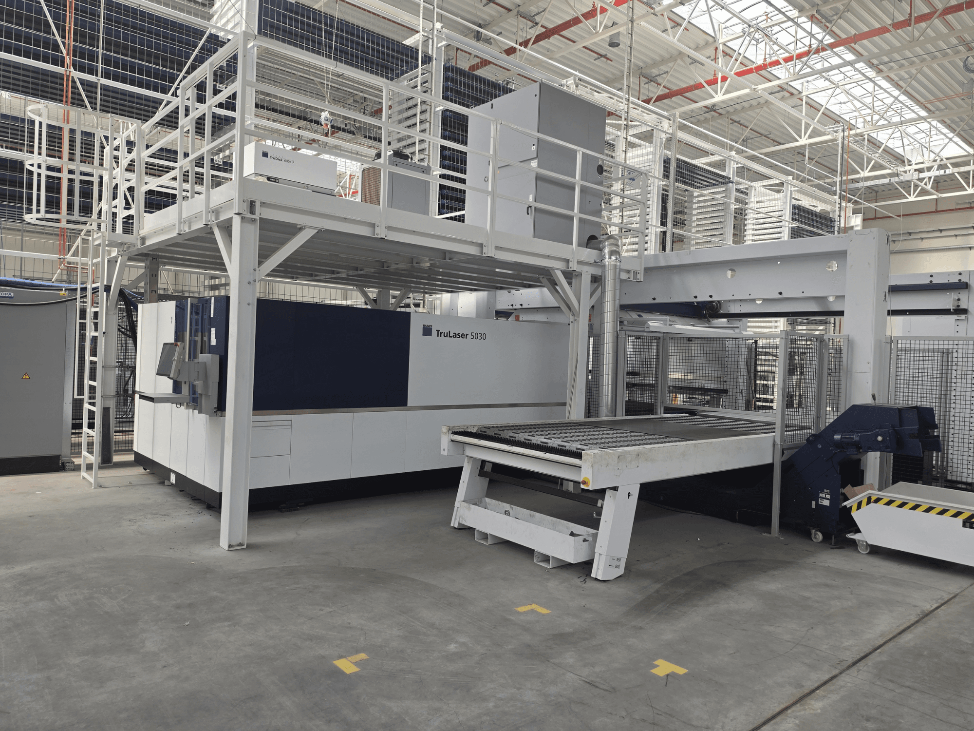 En TRUMPF TruLaser 5030 fiber L76 FMC-maskin i en verkstad, framifrån sett med skärområdet och in- och urlastningsmekanismen.
