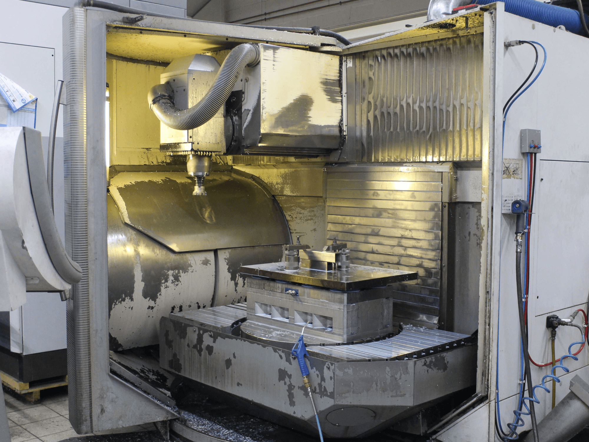 CNC-fräsmaskin, interiör, sidovy, visar arbetsstycke och skärverktyg med metallspån och rester av kylvätska.