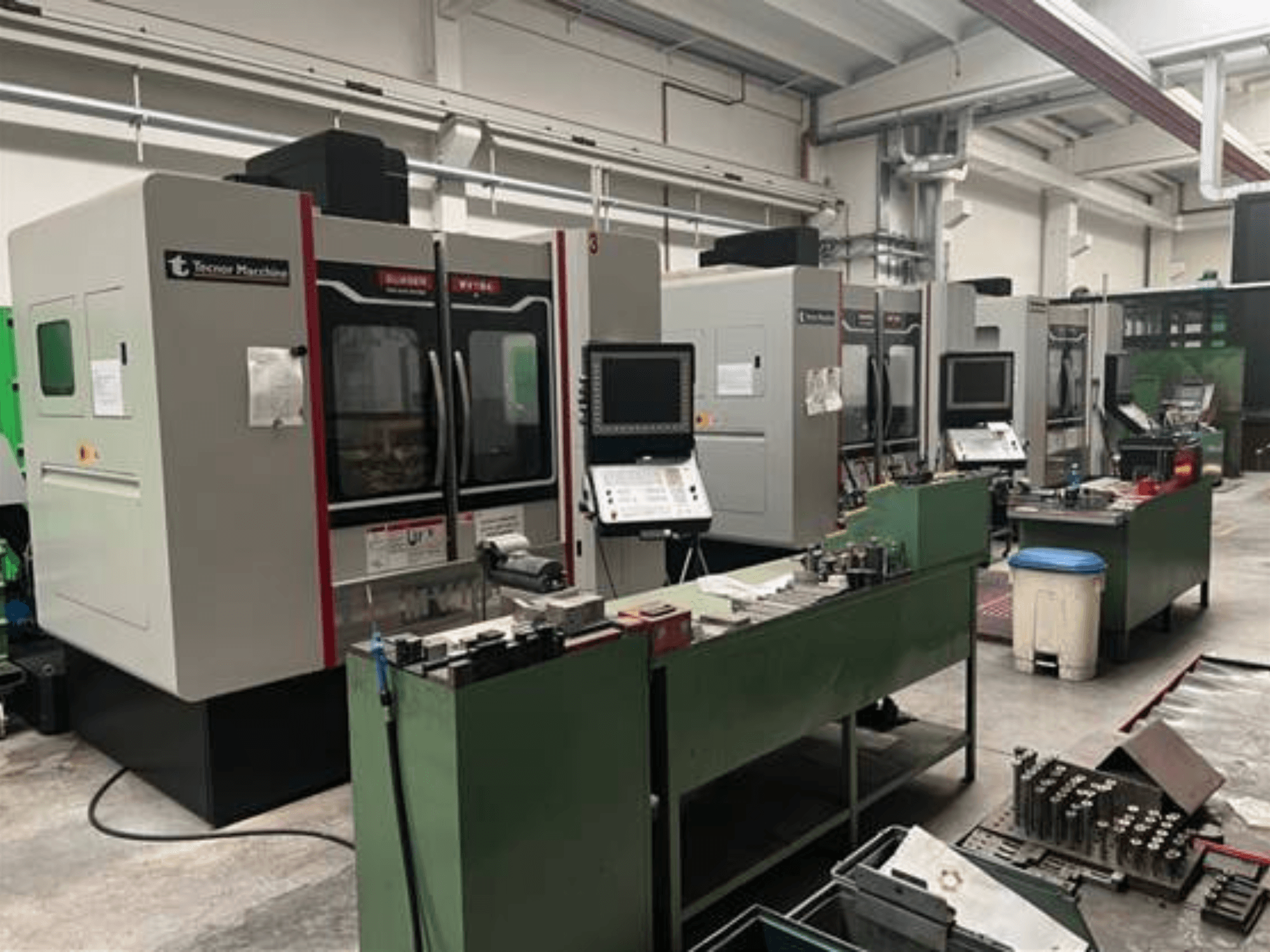 Fyra CNC-maskiner från Tecnoer Marchine i en verkstad, vy framifrån, med verktyg och delar på gröna arbetsbänkar.
