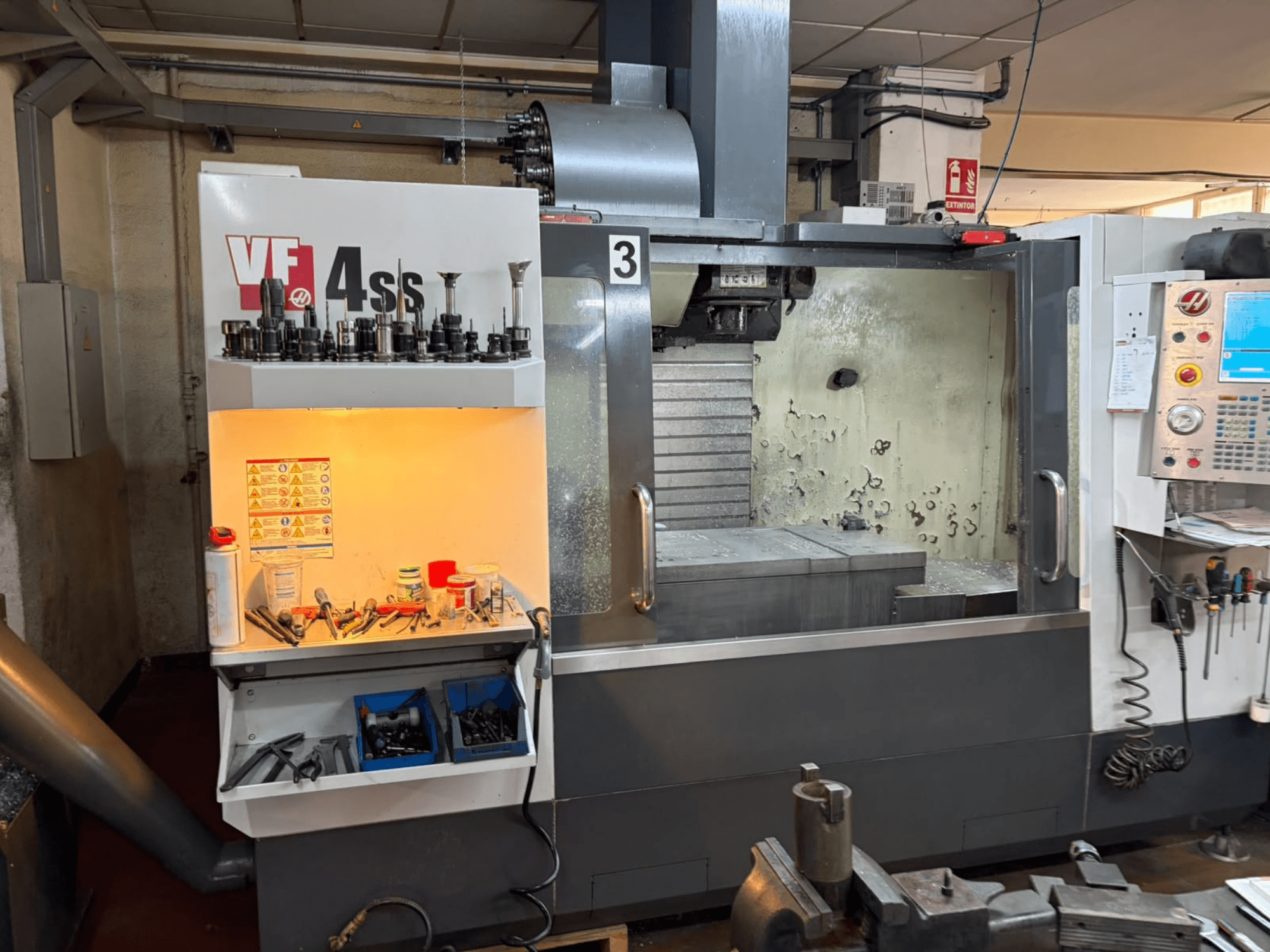 HAAS VP 4SS vertikalt bearbetningscenter, framifrån, med verktygsförvaring, kontrollpanel och synligt arbetsområde med detaljer om bearbetningen.
