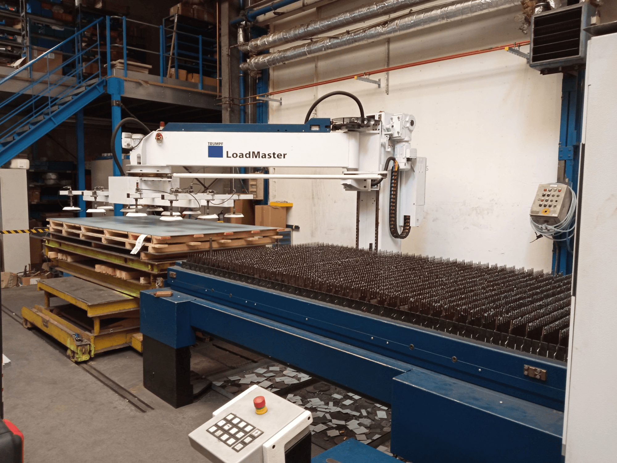 TRUMPF TruLaser 3030 CO₂-laserskärmaskin sett från sidan, med en LoadMaster och pallar med material.