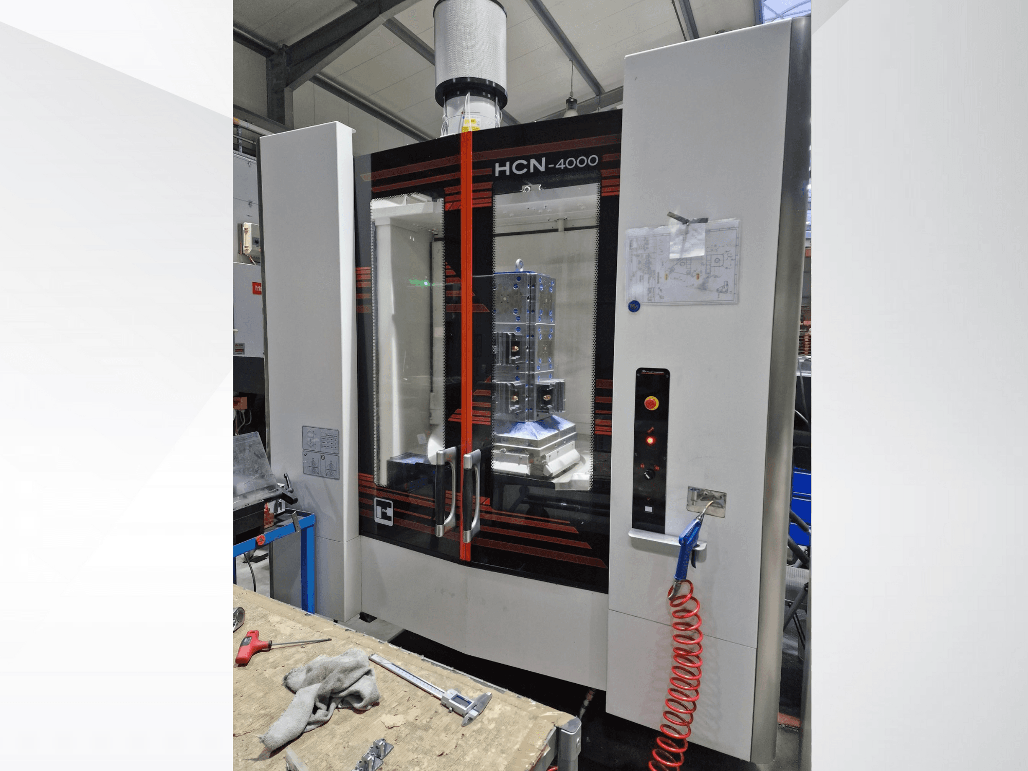 HCN-4000 CNC-maskin framifrån, med glaspanel, kontrollpanel med knappar och en bifogad ritning.