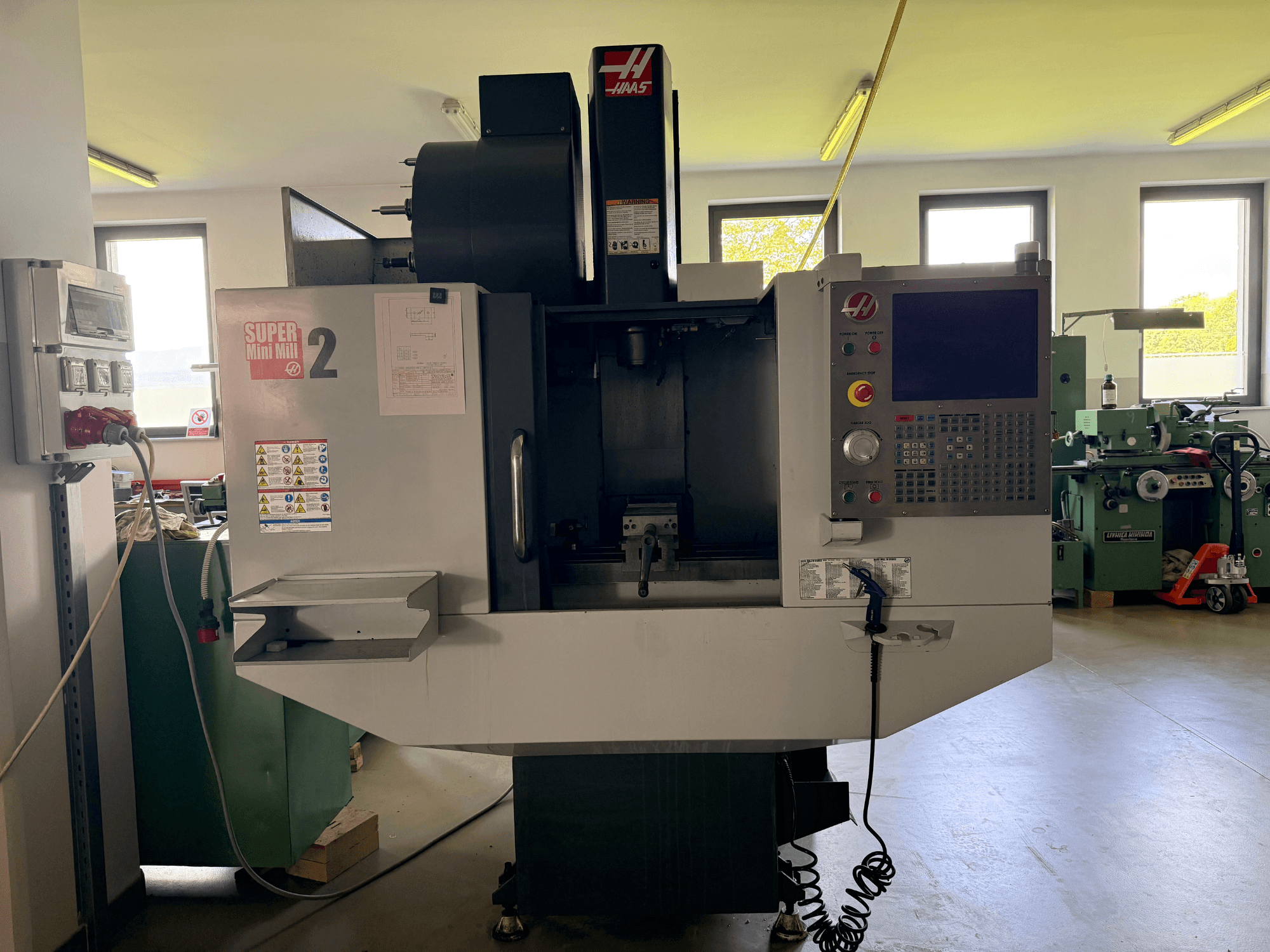 Haas Mini Mill 2 vertikala fleroperationsmaskin framifrån, med kontrollpanel och verktygsområde med varningsetiketter.
