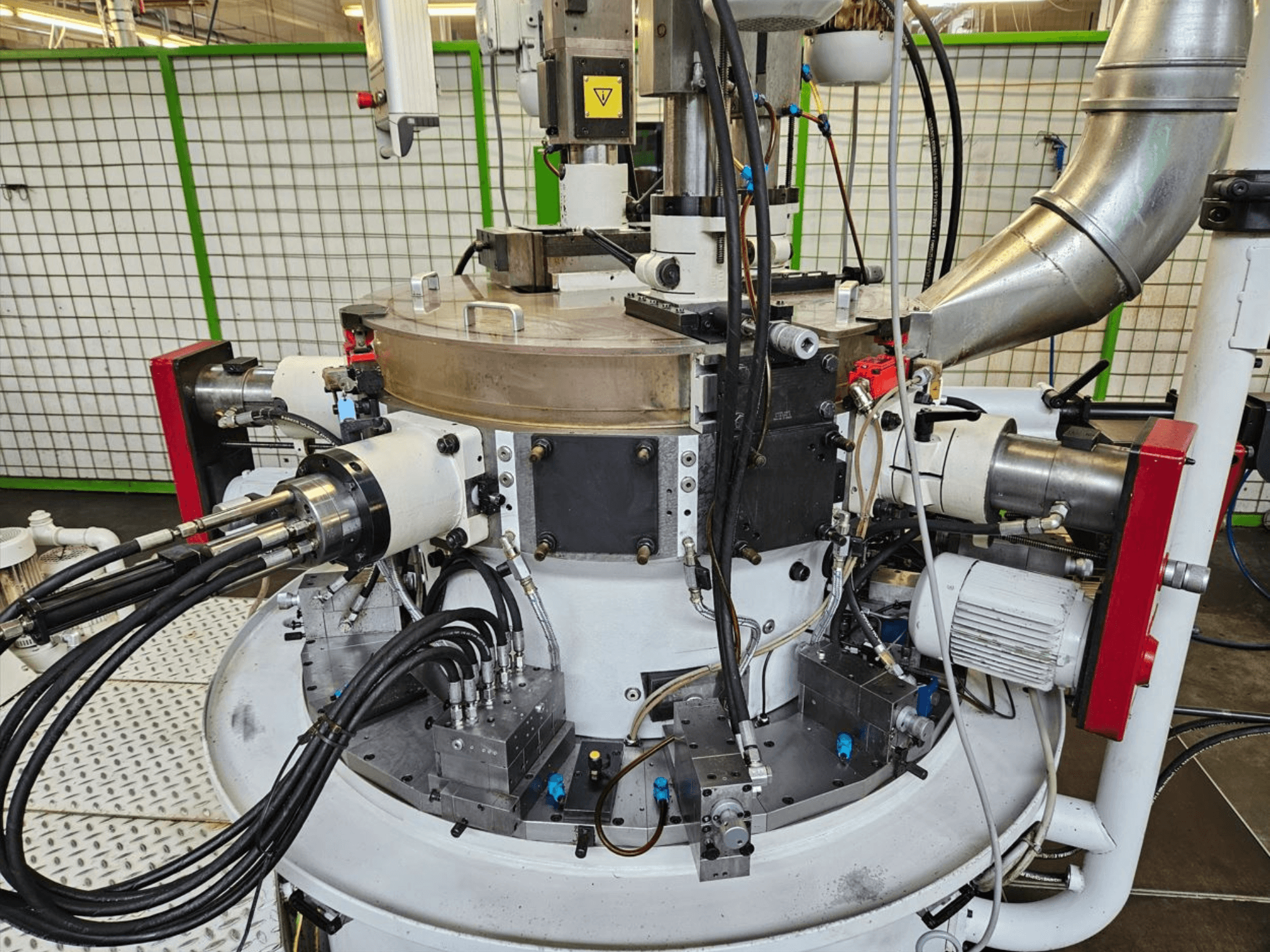 Närbild av en industrimaskin med hydraulslangar, metallkomponenter och roterande bas. Inget varumärke synligt.