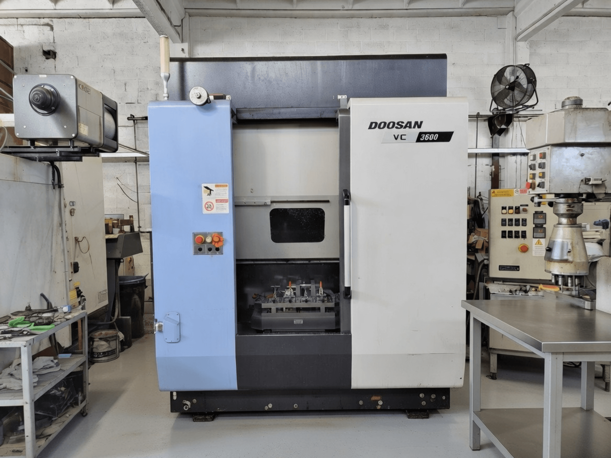 DOOSAN VC 3600 vertikal fleroperationsmaskin framifrån, med kontrollpanel och öppen dörr som visar arbetsutrymmet.
