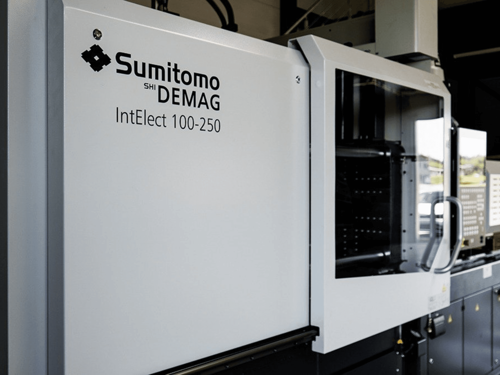 Framifrån sett: SUMITOMO SHI DEMAG IntElect 100/250, en elektrisk formsprutningsmaskin med kontrollpanel och säkerhetsfunktioner.