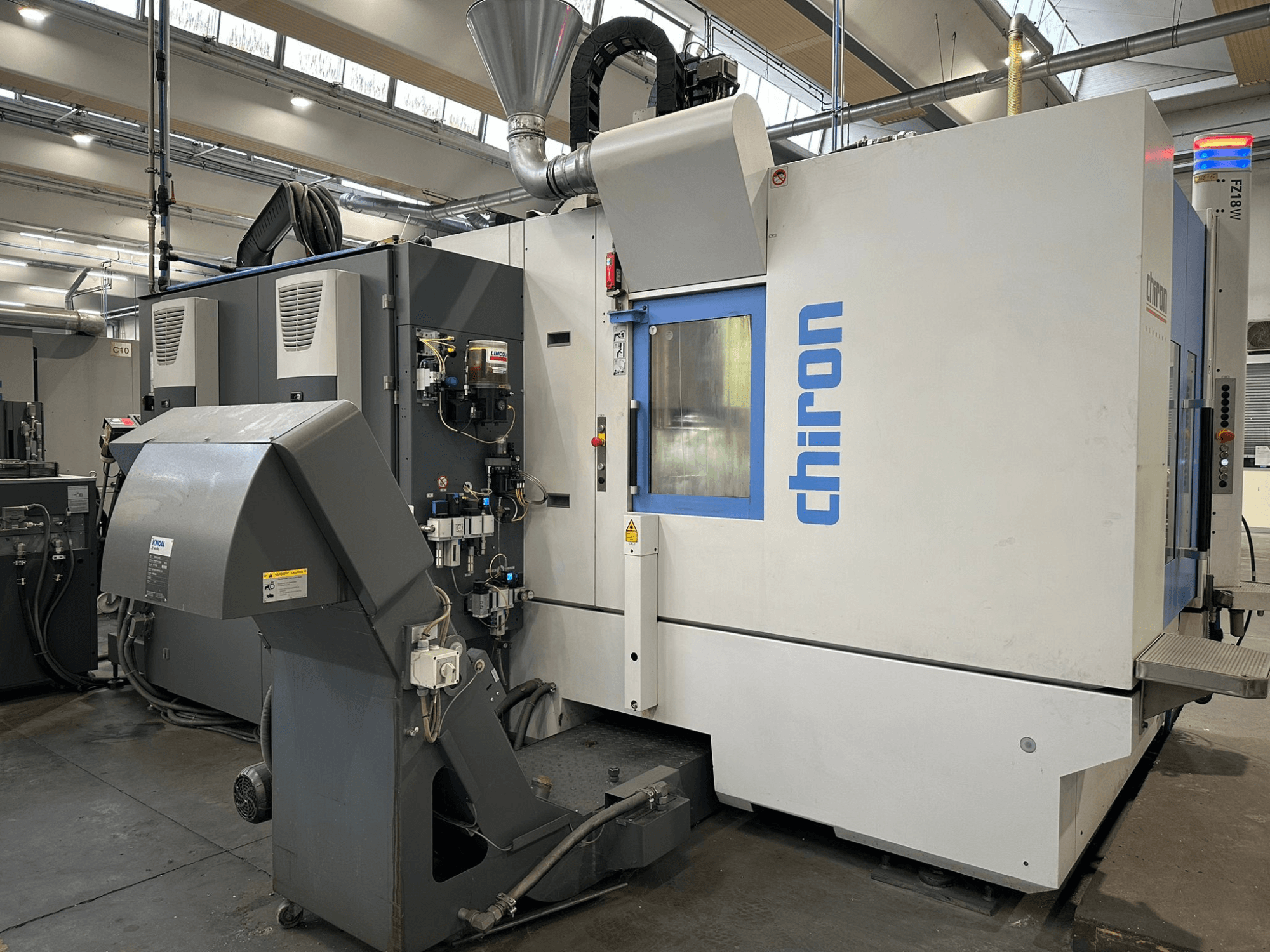 CNC-maskin Chiron i grått och vitt, framifrån, med reglage, rör och dammutsugningshuv.