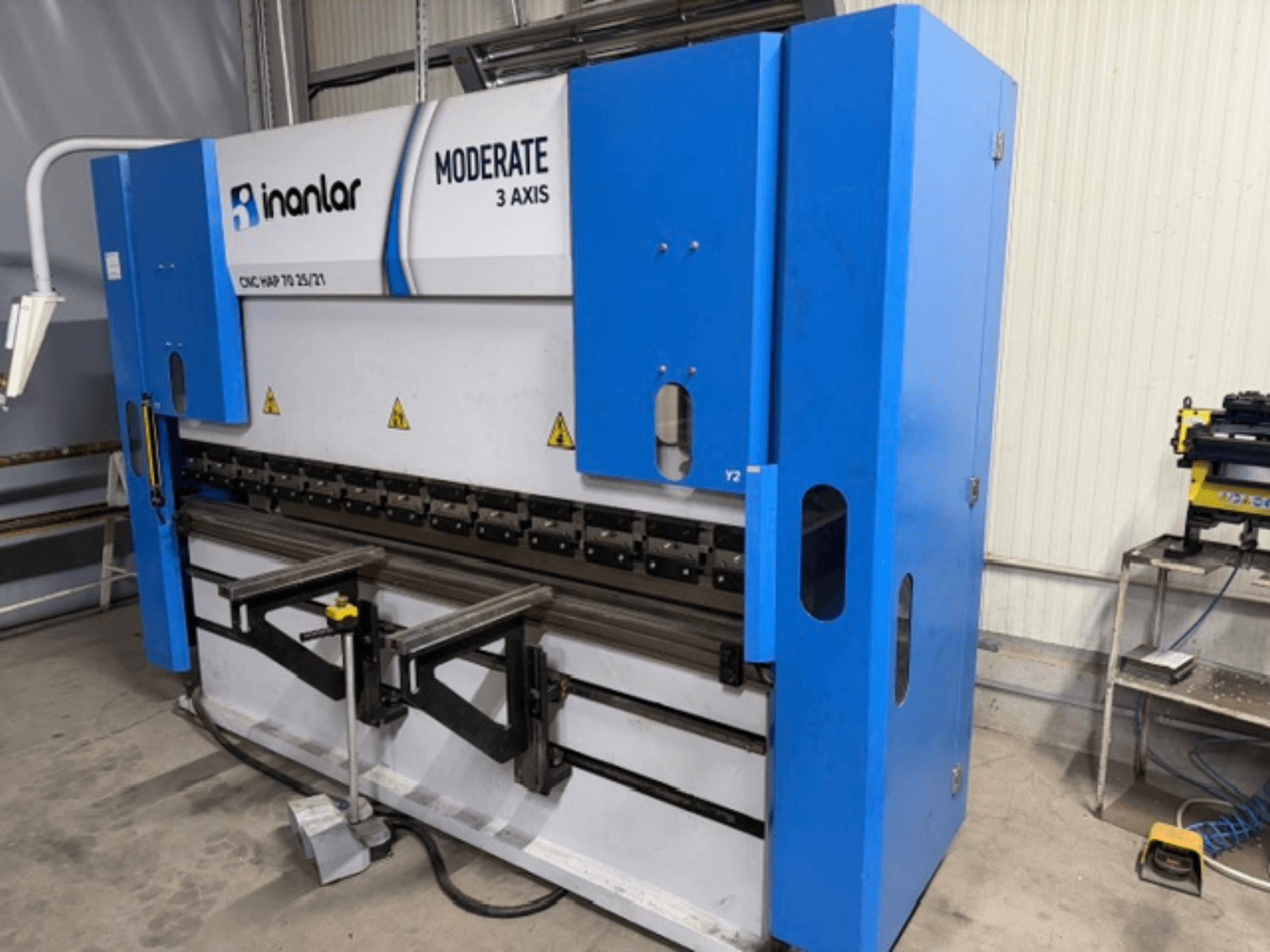 Inanlar Moderat 3-axlig CNC-maskin i blått, framifrån, med manöverspakar och säkerhetsetiketter synliga på kroppen.