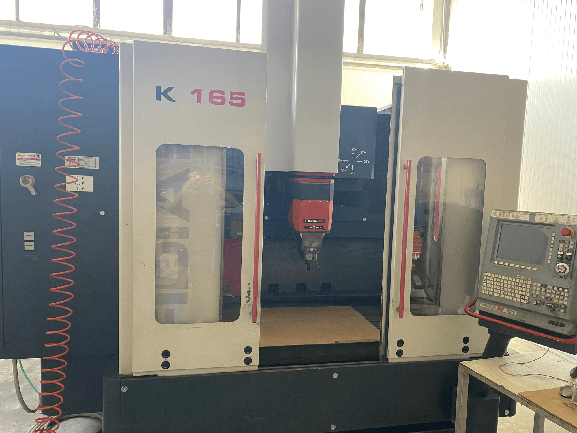 Fidia K 165 CNC-maskin med röd spindel och kontrollpanel, sedd framifrån i en väl upplyst verkstadsmiljö.