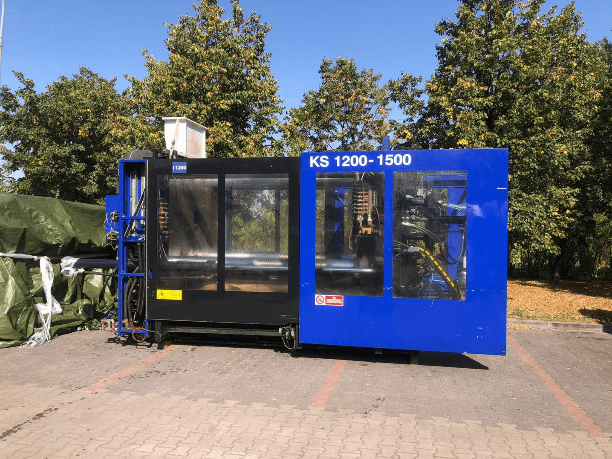 Hydraulisk formsprutningsmaskin ITALTECH KS 1200 8300 ES, sidovy, som visar reglage och maskindetaljer i en parkmiljö.