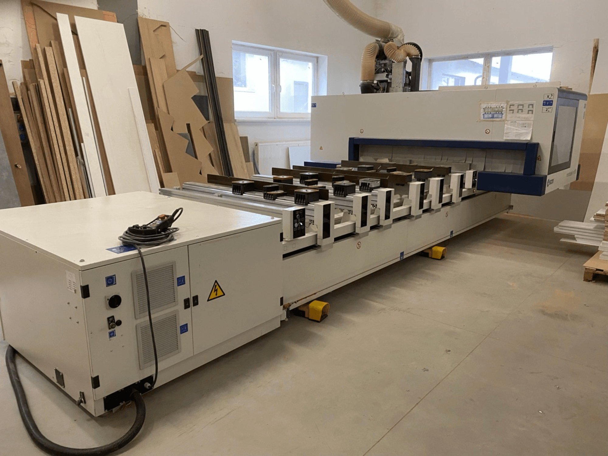 SCM Morbidelli: Bild på CNC-bearbetningscentret M100 för träbearbetning i en verkstad, som visar en framifrånvy med kontrollpanel och dammutsug.