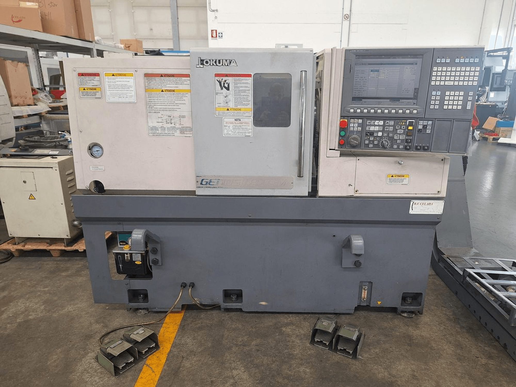 Okuma GENOS L200E-M horisontell svarv i sidovy; har kontrollpanel, säkerhetsvarningar och fotpedaler.